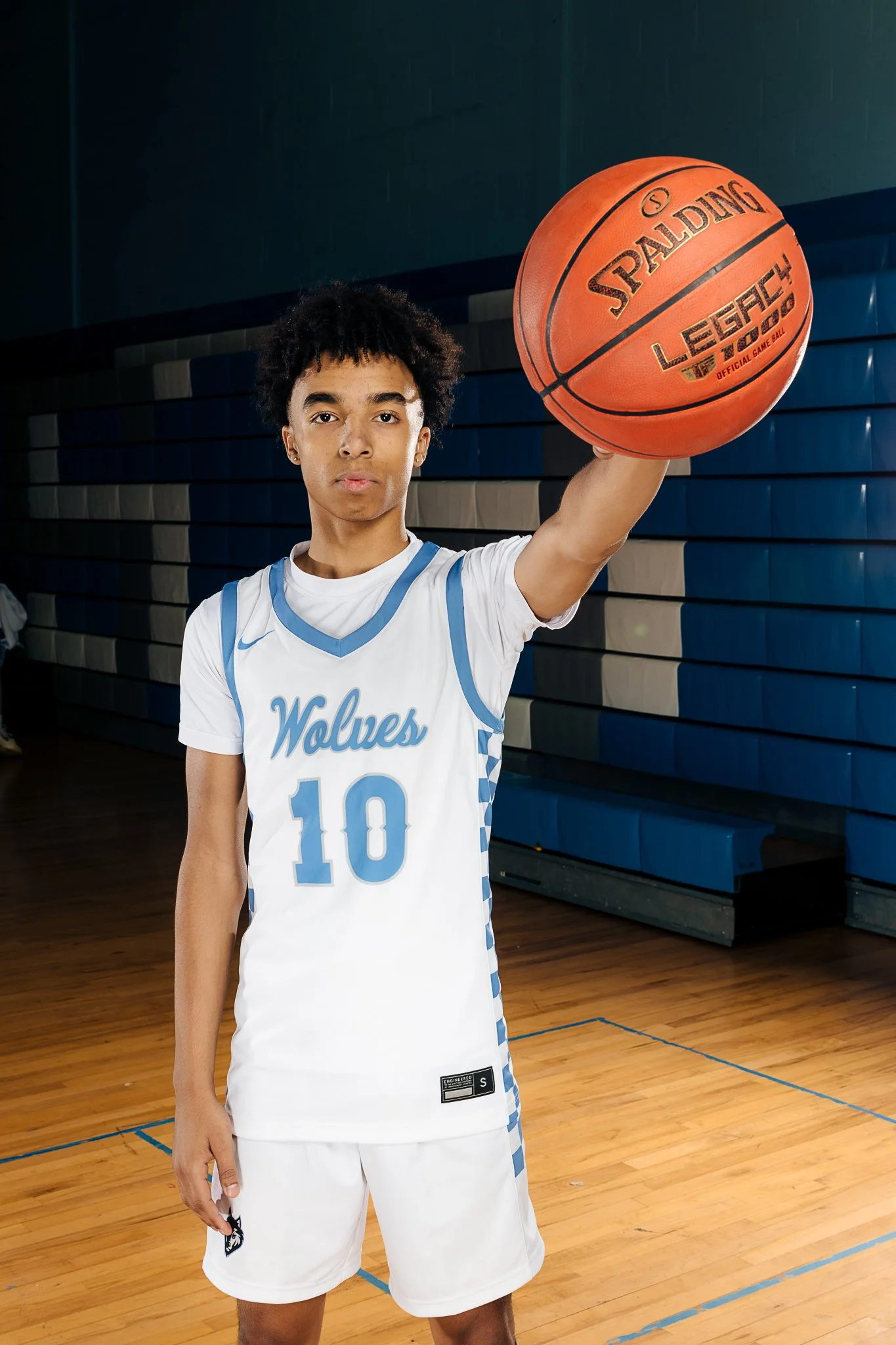 A young basketball player in a white and blue uniform with the number 10 and 'Wolves' written on it, holding a basketball in an indoor gym.