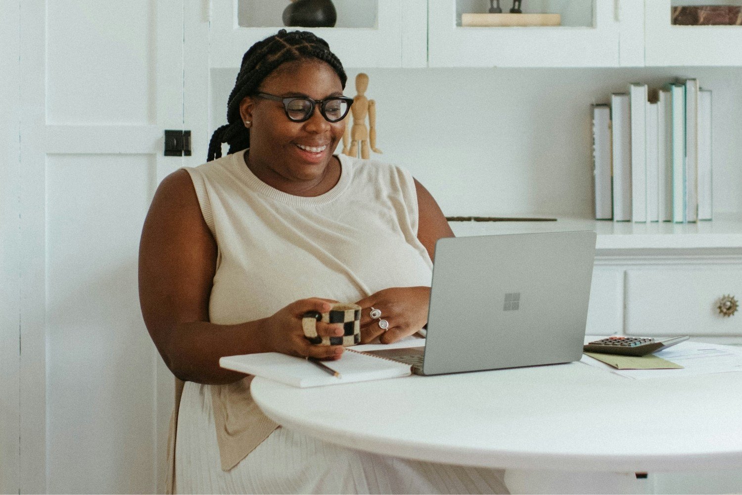 Smiling professional woman working comfortably at a home desk with a laptop and coffee, representing the freedom and focus leaders gain with Ezer VA Group.