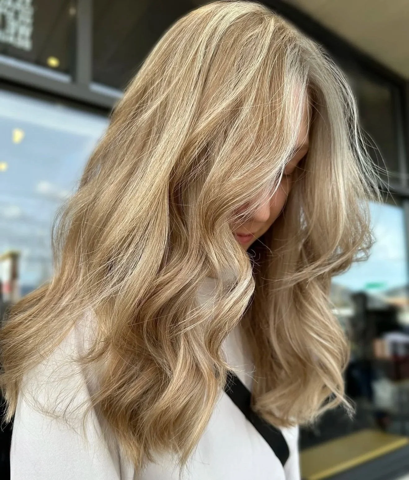 Close-up of blonde, wavy hair on a woman with her head tilted downward, in an indoor setting.