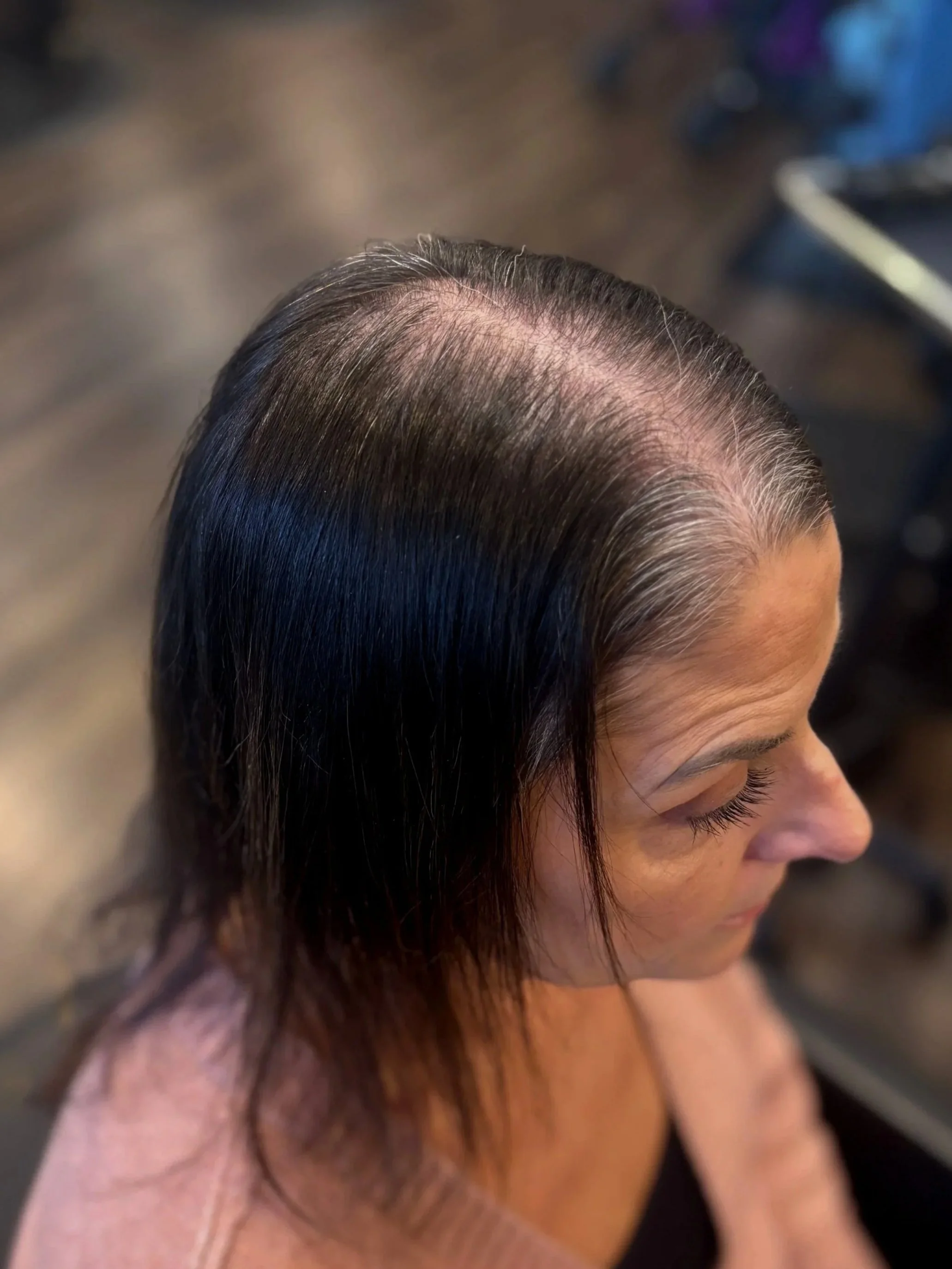 A woman with short, dark, and graying hair, showing a recent haircut with the top styled back and sides cut shorter, seated in a salon chair.