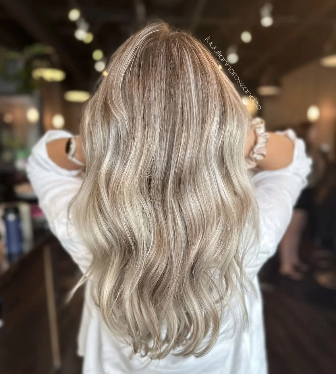 Back view of a woman with long, wavy blonde hair in a salon or similar setting.