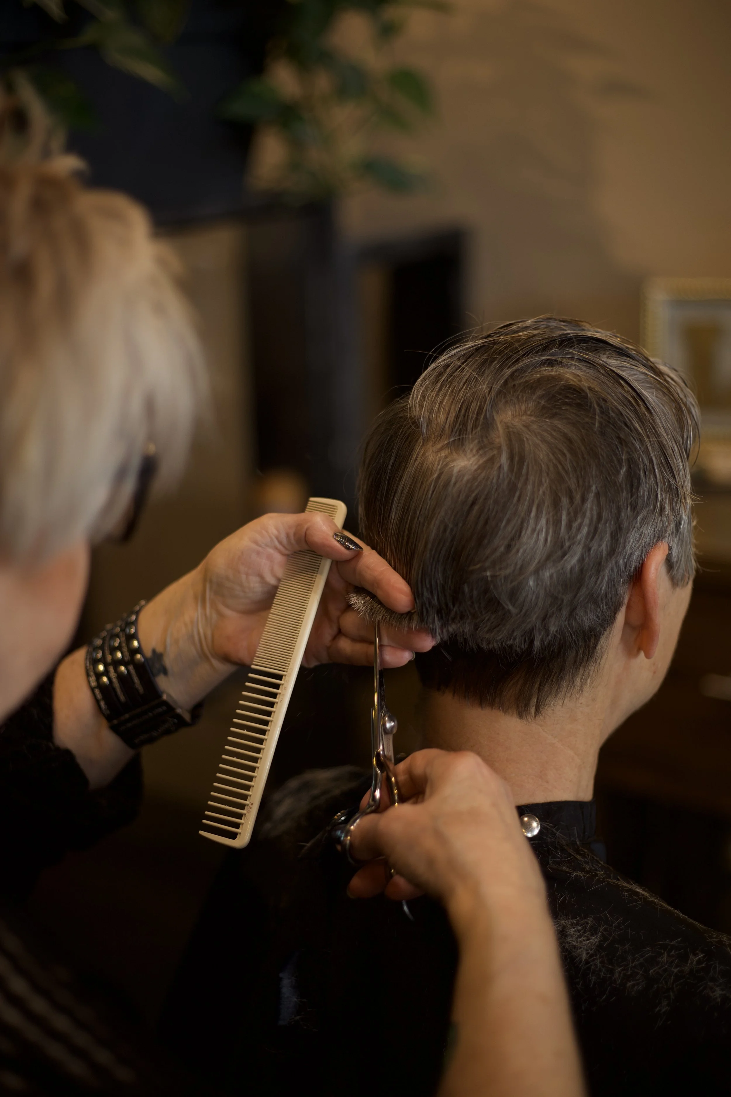 A hairstylist cutting a man's hair with scissors and comb inside a salon.