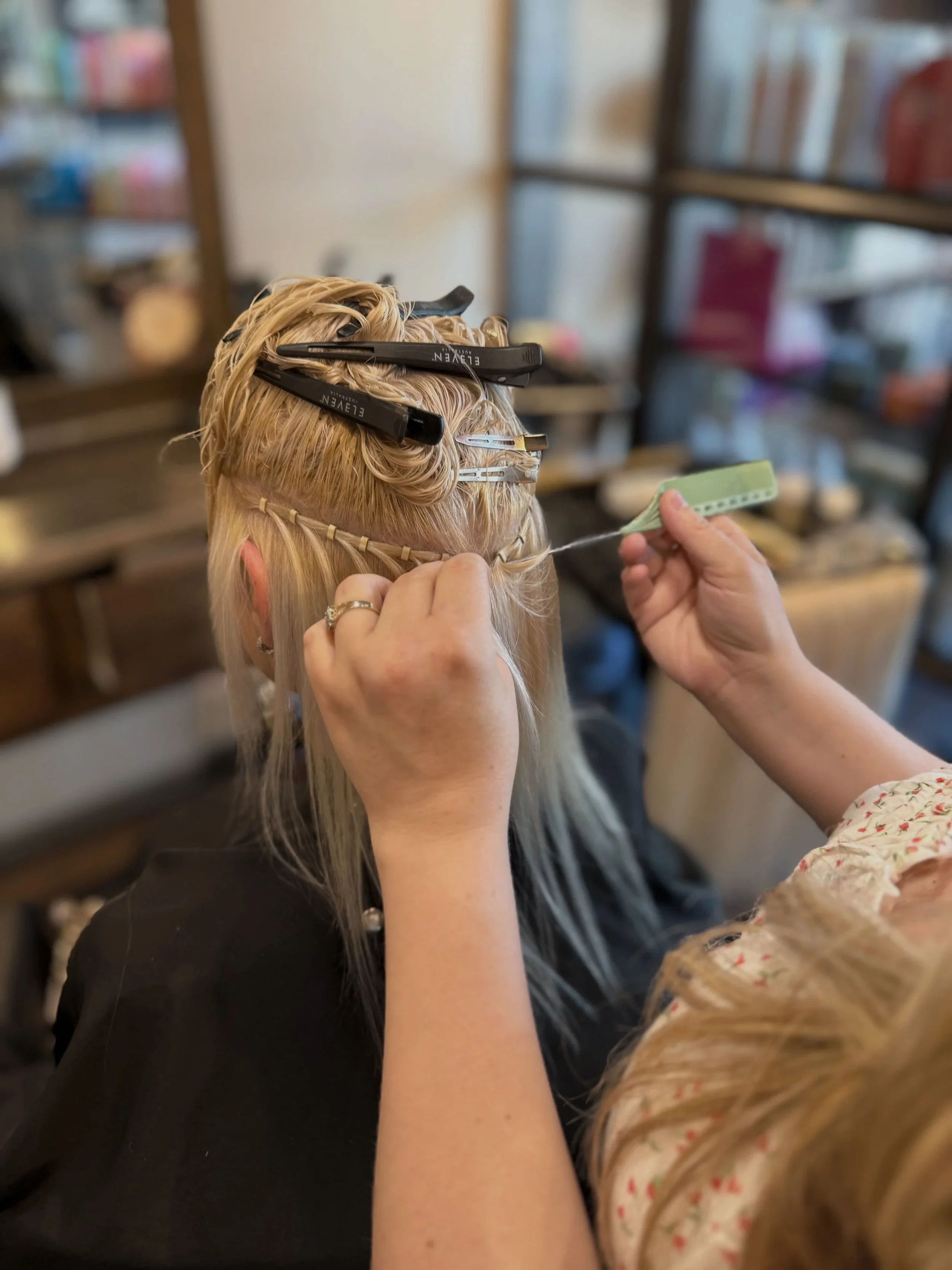 Person getting their blonde hair styled with section clips, hair is held with a green hair sectioning clip, in a salon setting.