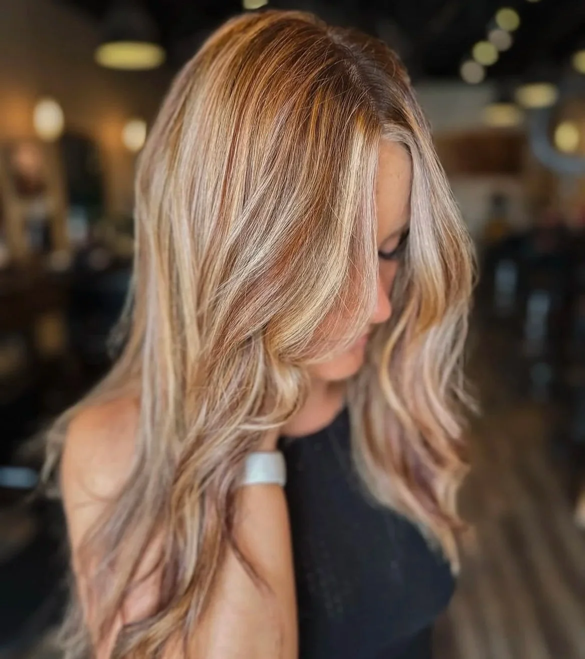 Side view of a woman with long, wavy blonde hair in a salon or restaurant setting.