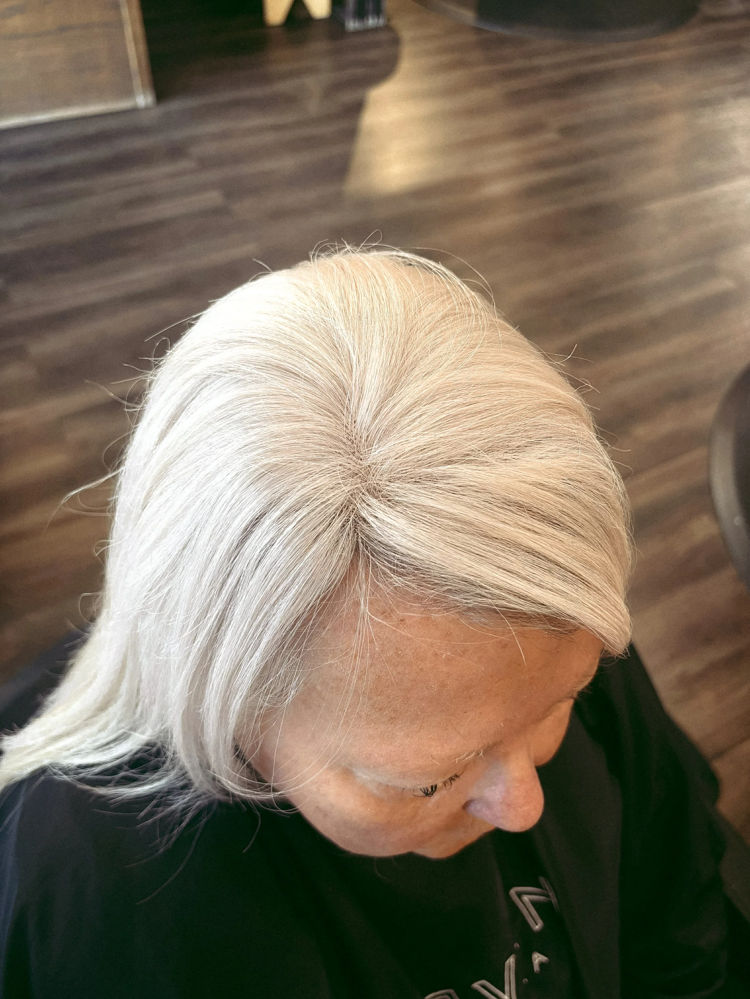 Top-down view of a woman with long silver hair sitting in a room with dark wood flooring.
