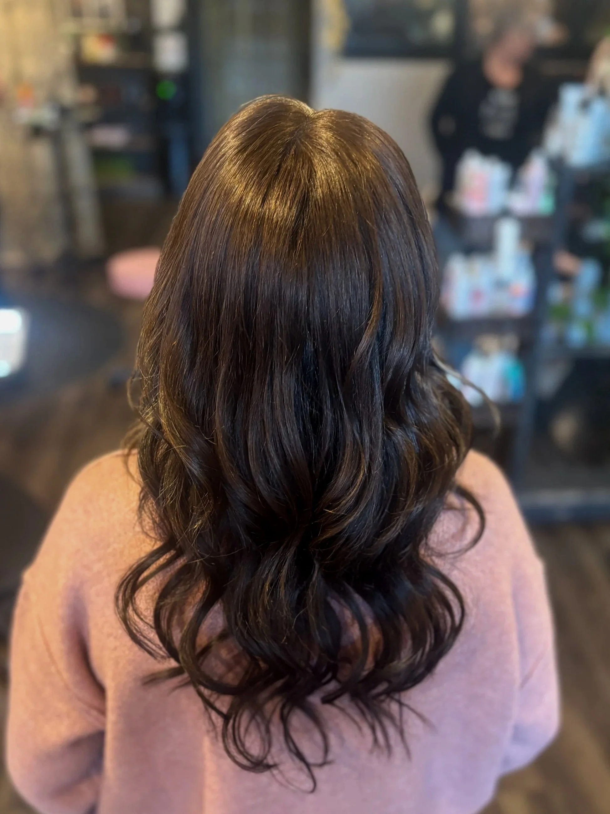 Back of woman with long, dark, wavy hair in a salon or similar setting.