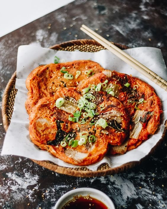 Korean kimchi pancakes garnished with green onions on a plate with chopsticks; dipping sauce on the side.