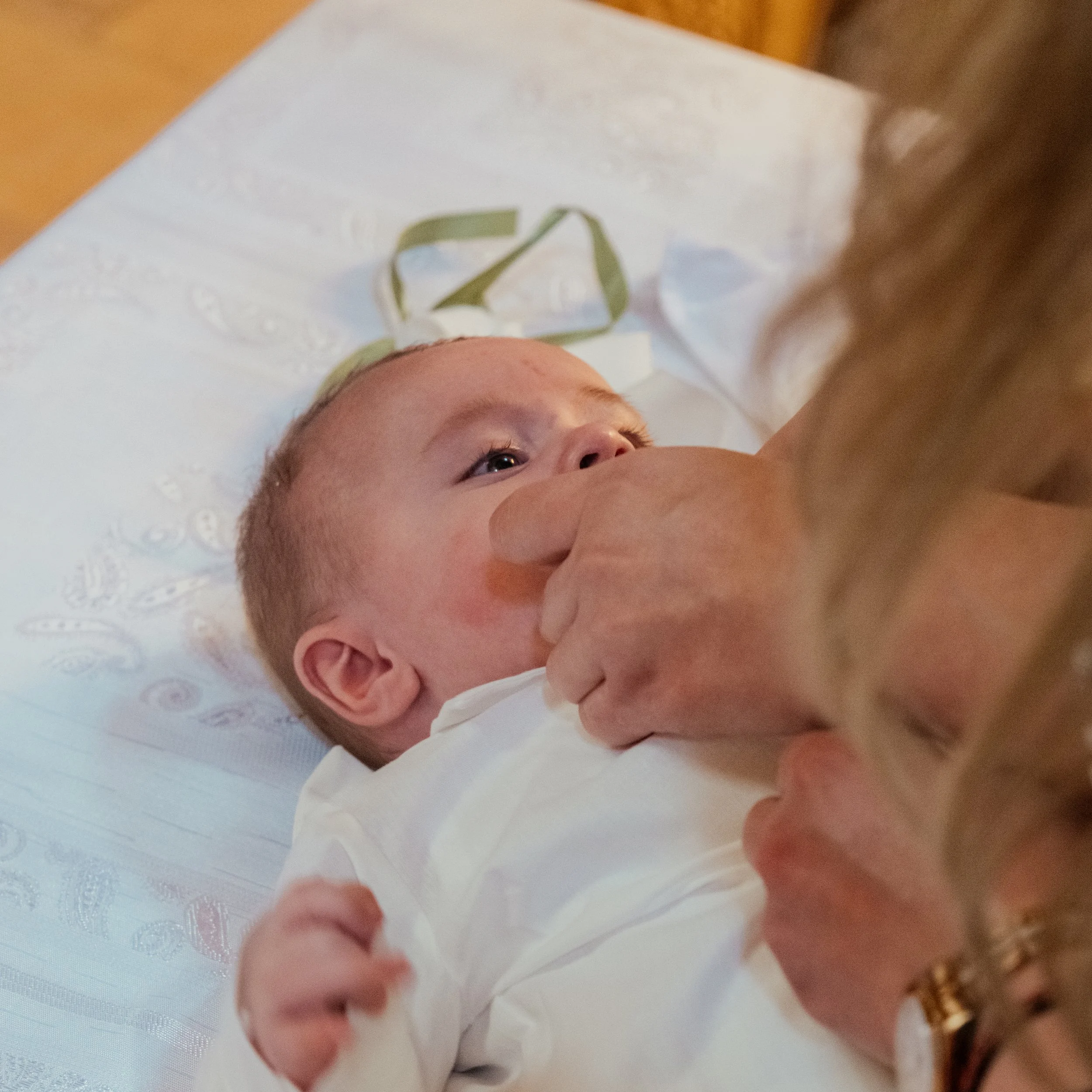 Close-up of a baby lying on a white textured blanket, looking up at the camera with wide eyes and expressive face.