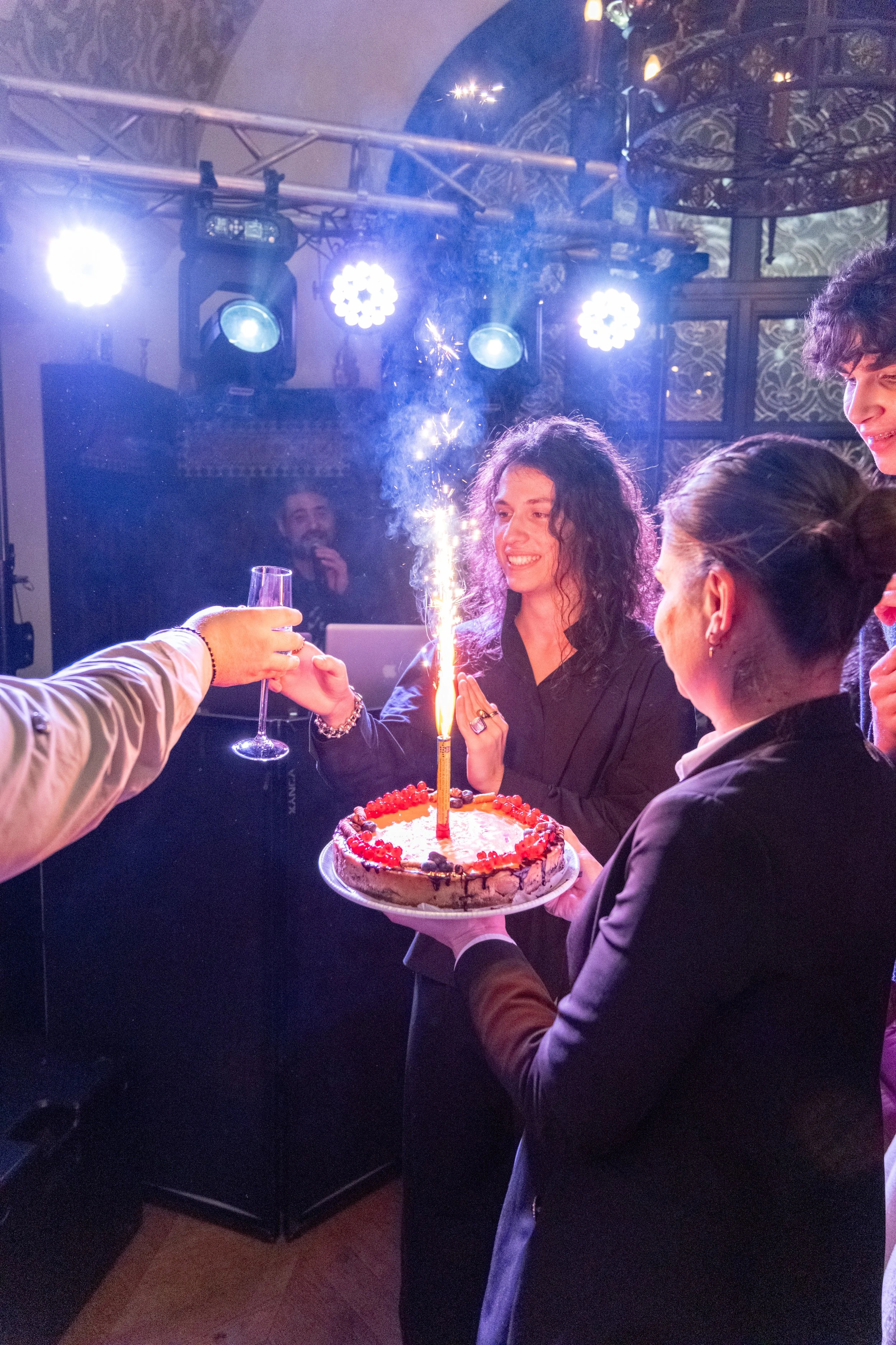 People celebrating a birthday with cake and sparklers in a dimly lit room with stage lighting.