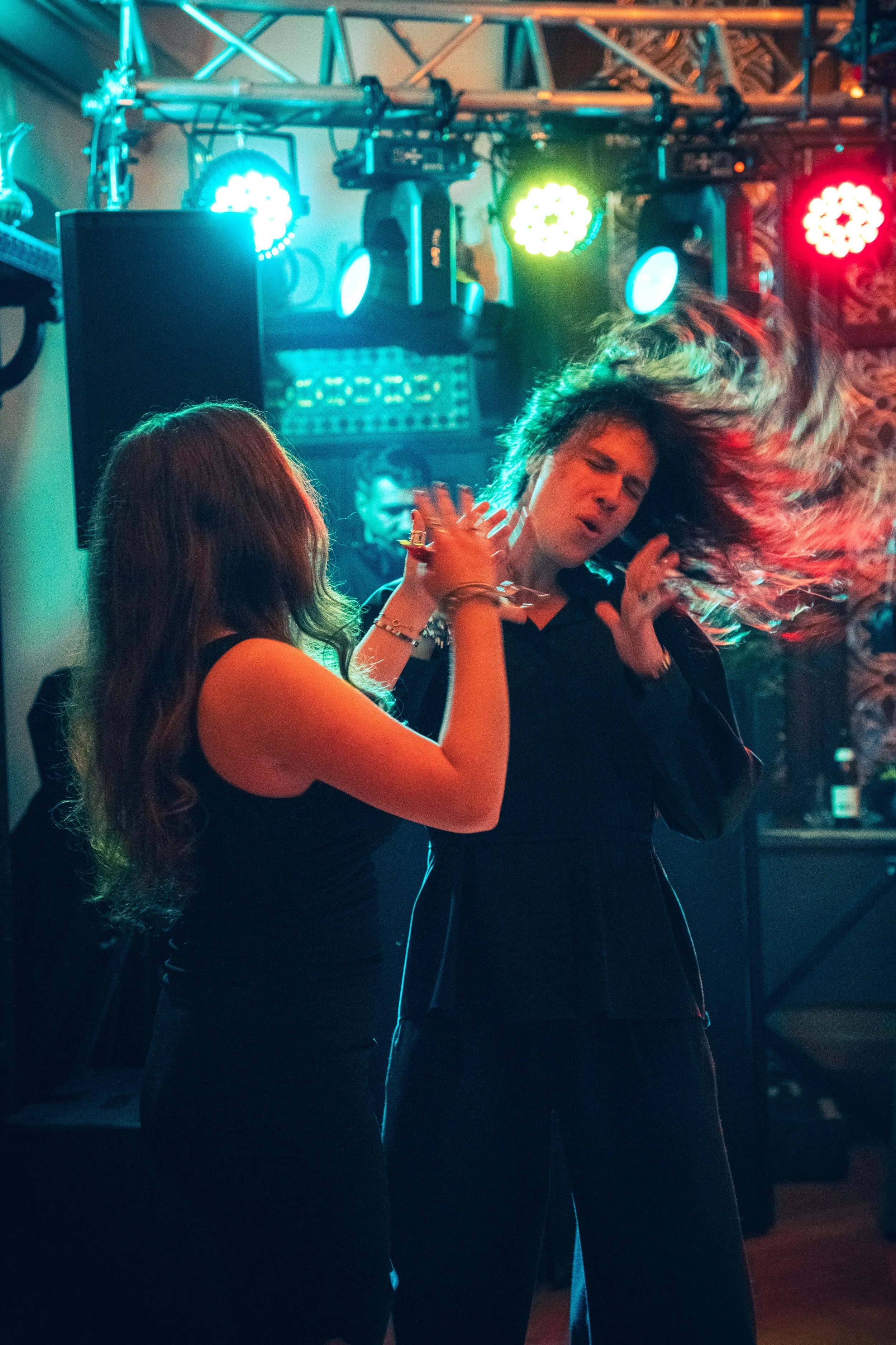 Two women dancing close together in a nightclub with colorful stage lights in the background.