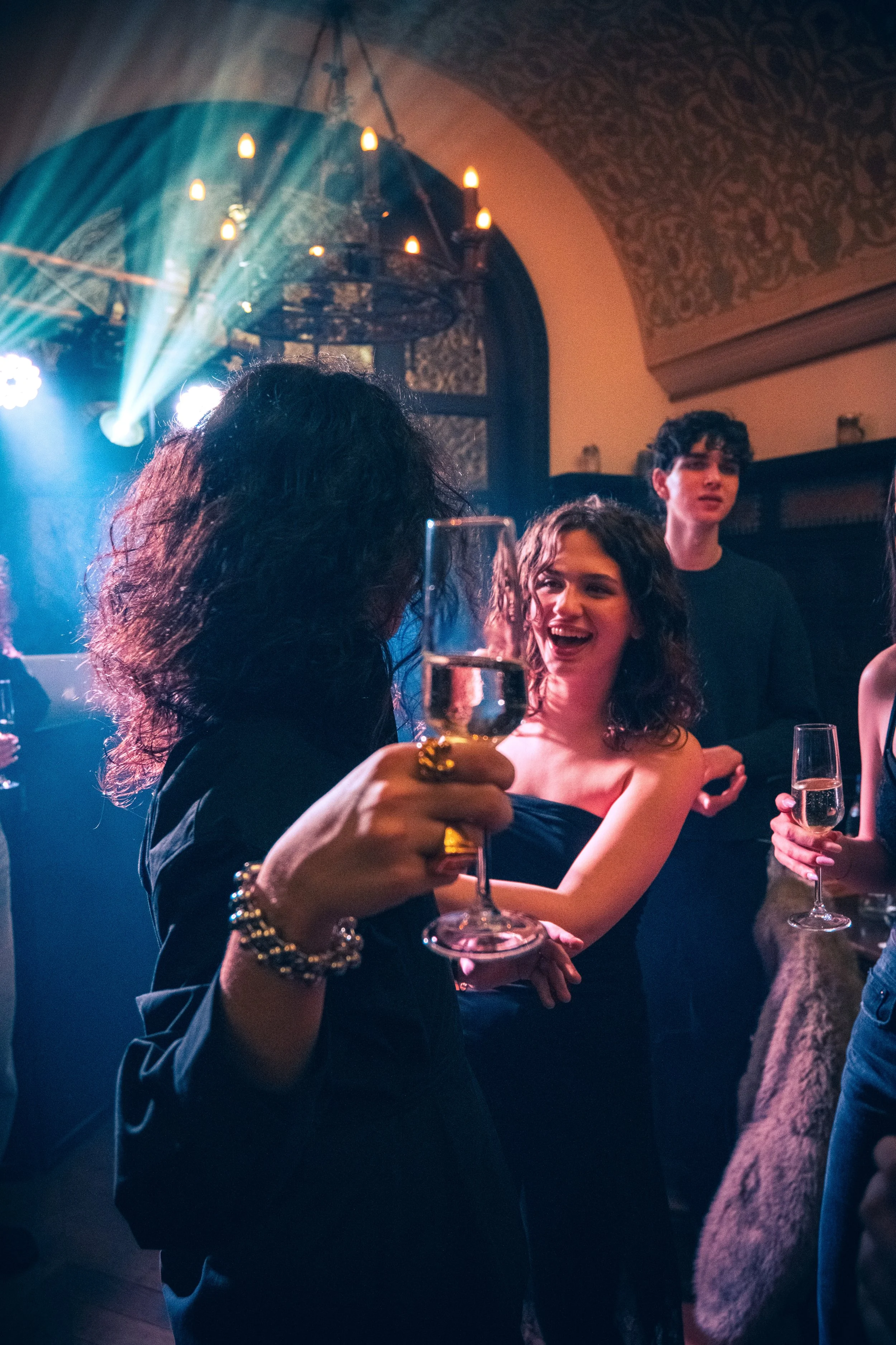 People celebrating with glasses of champagne at a party with colorful lighting and a decorative ceiling.
