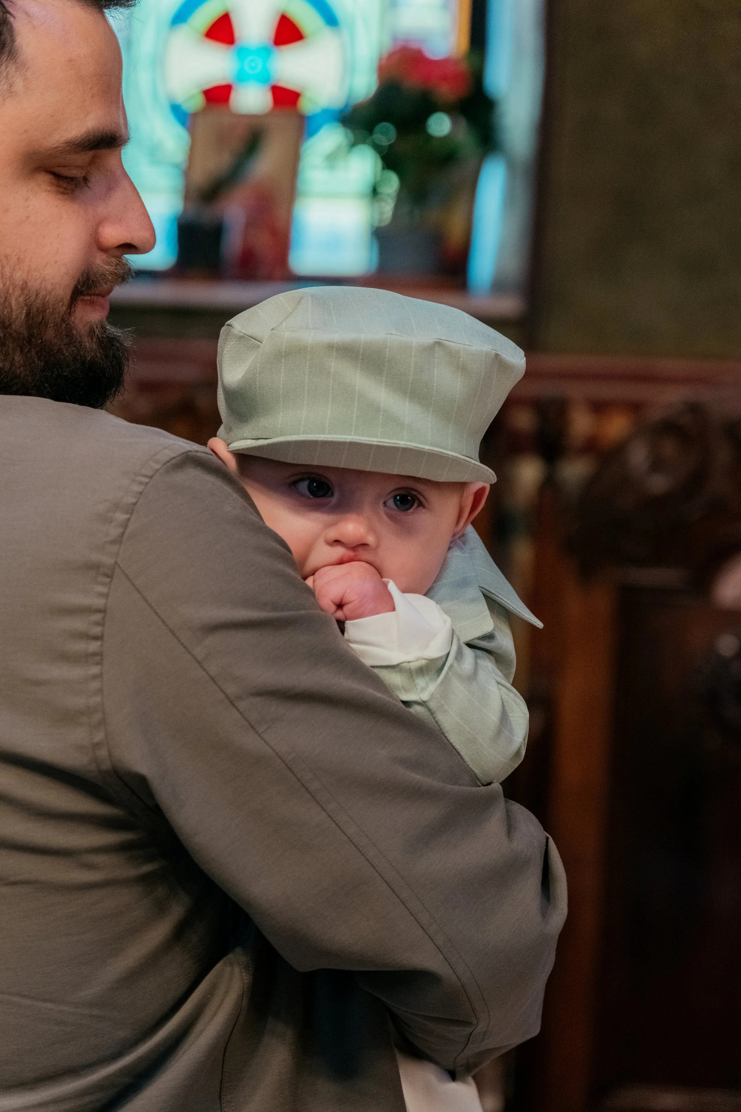 A man with a beard and closed eyes holding a young child with a light-colored cap, in a cozy indoor setting with blurred holiday decorations in the background.