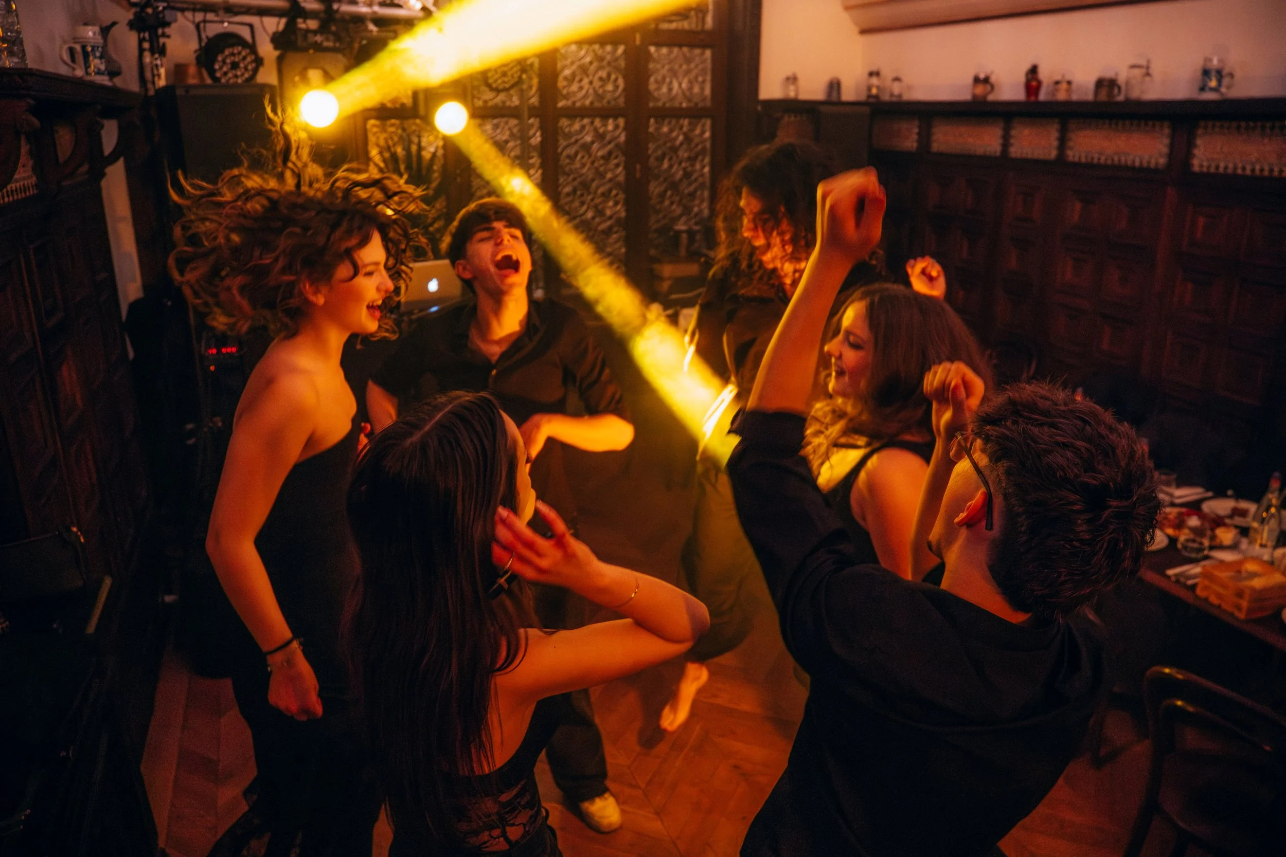 People dancing and enjoying music in a dimly lit indoor setting with warm lighting and wooden decor.