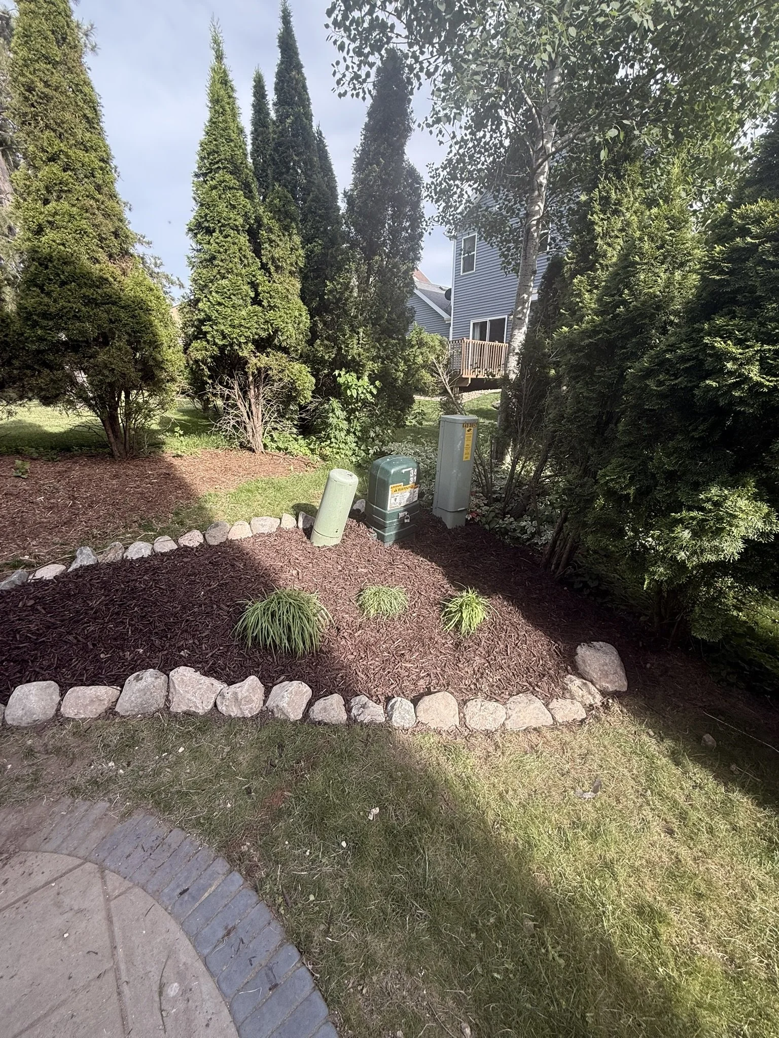Ornamental grasses planted around utility pedestals in a fieldstone-edged mulch bed in Madison, WI