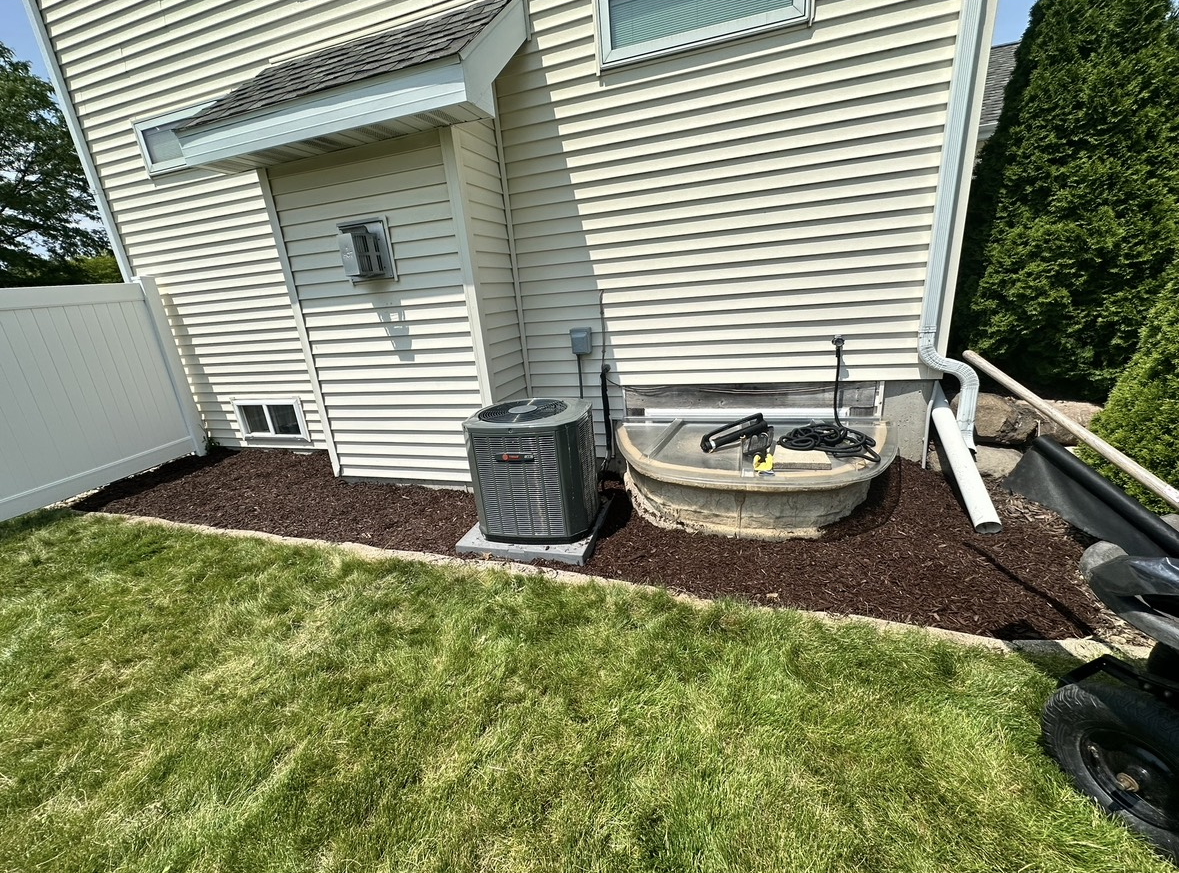 Front garden bed with fresh dark mulch inside a stone border, with the homeowner's garden ornaments — Sun Prairie, WI