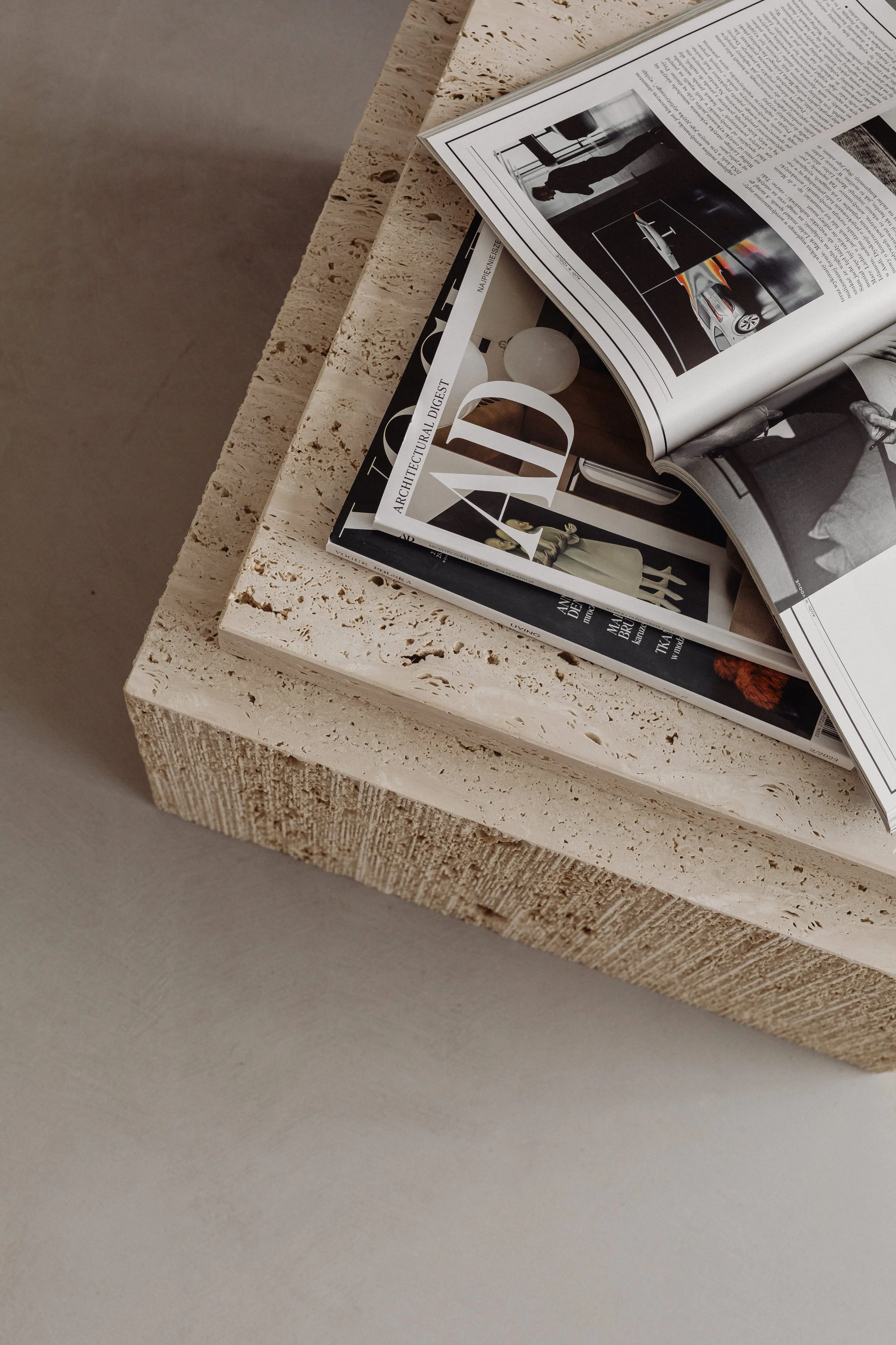 Stack of magazines on a textured light-colored stone coffee table, with some pages open.