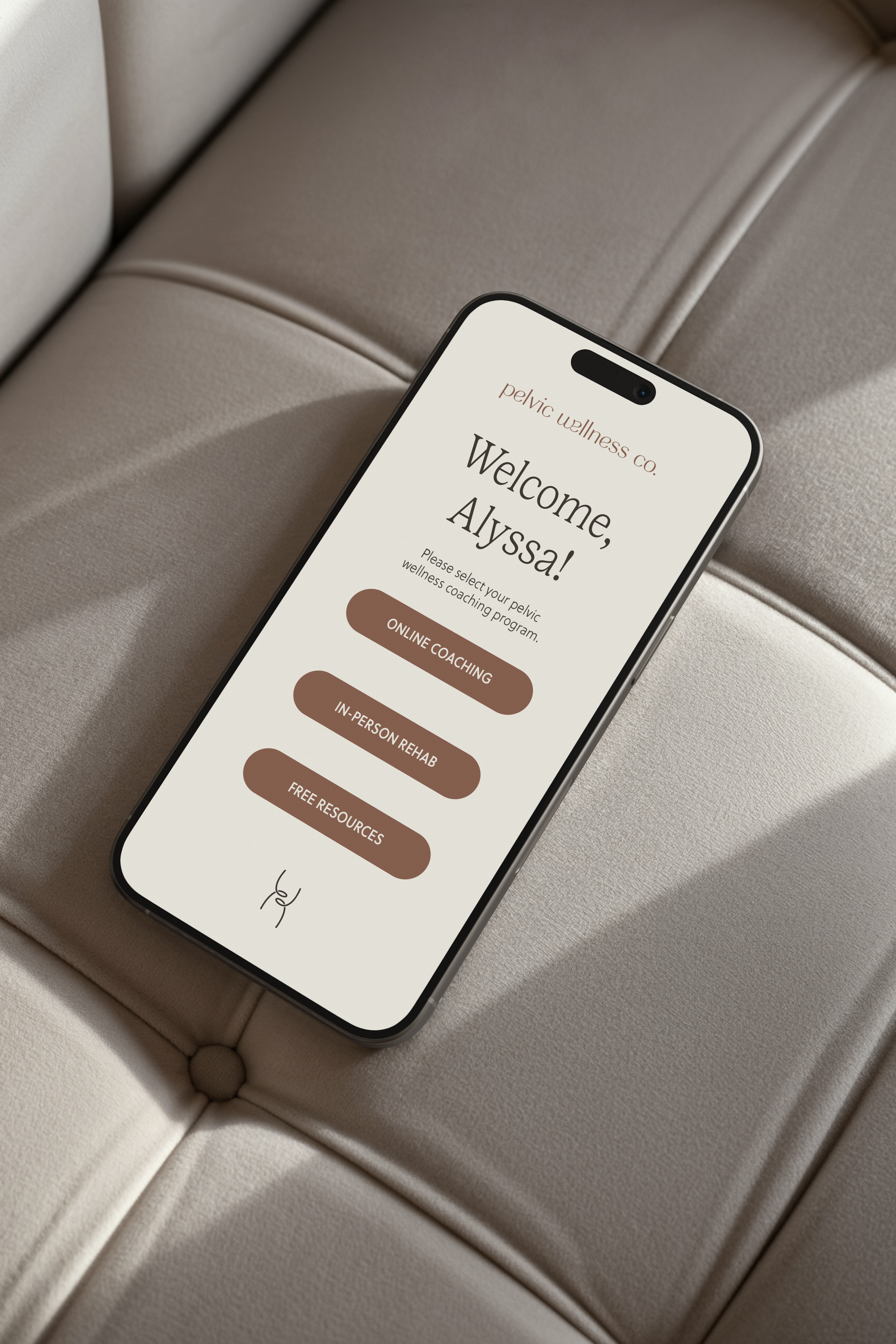 Smartphone displaying a welcome screen with Pelvic Wellness Co's logo, designed by Evelle Creative, with options for online coaching, in-person rehab, and free resources, resting on a beige leather surface.