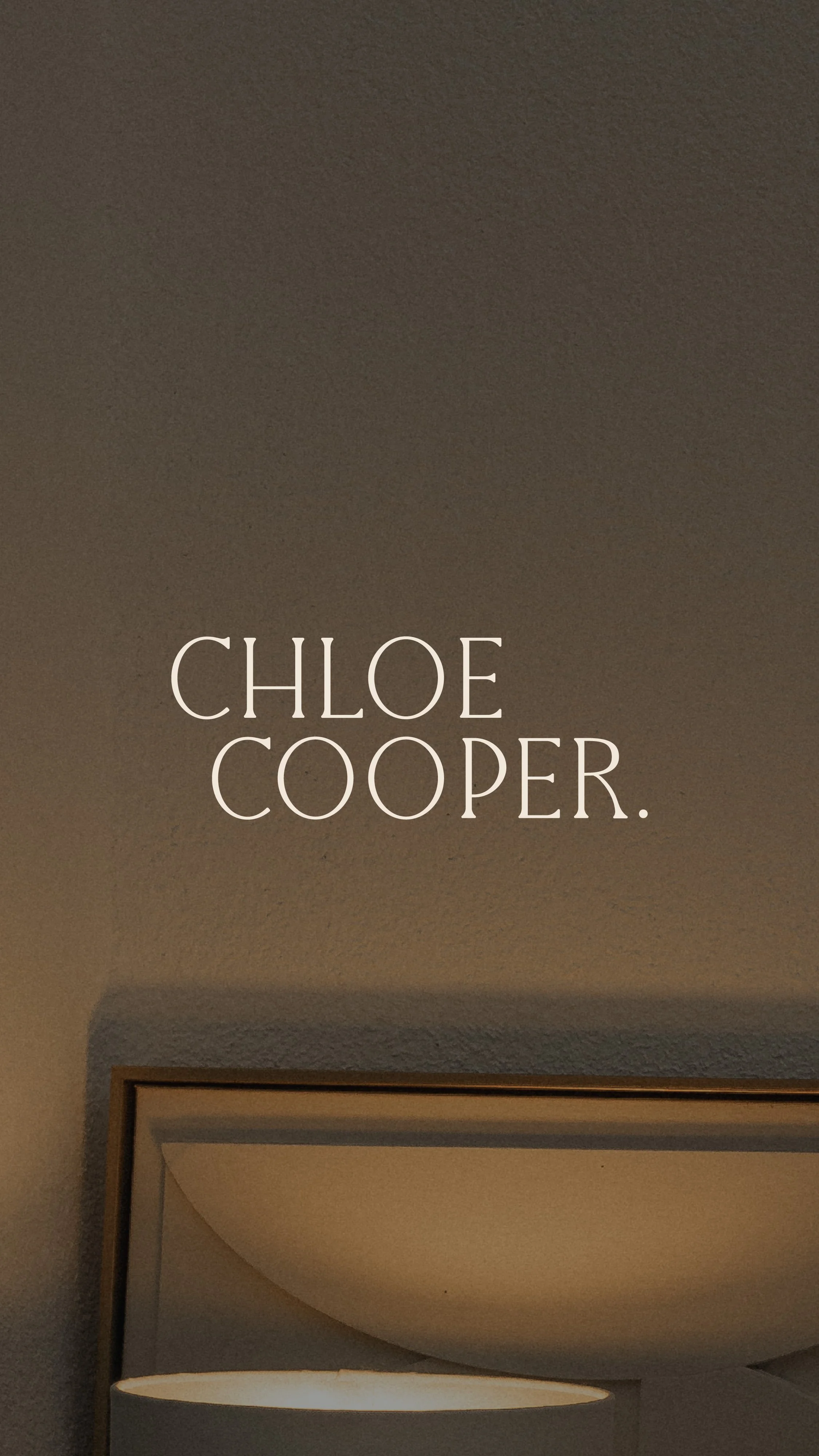 A plain wall with the words 'Chloe Cooper.' centered in large, elegant font, partially visible light fixture below, and it appears to be a modern interior space.