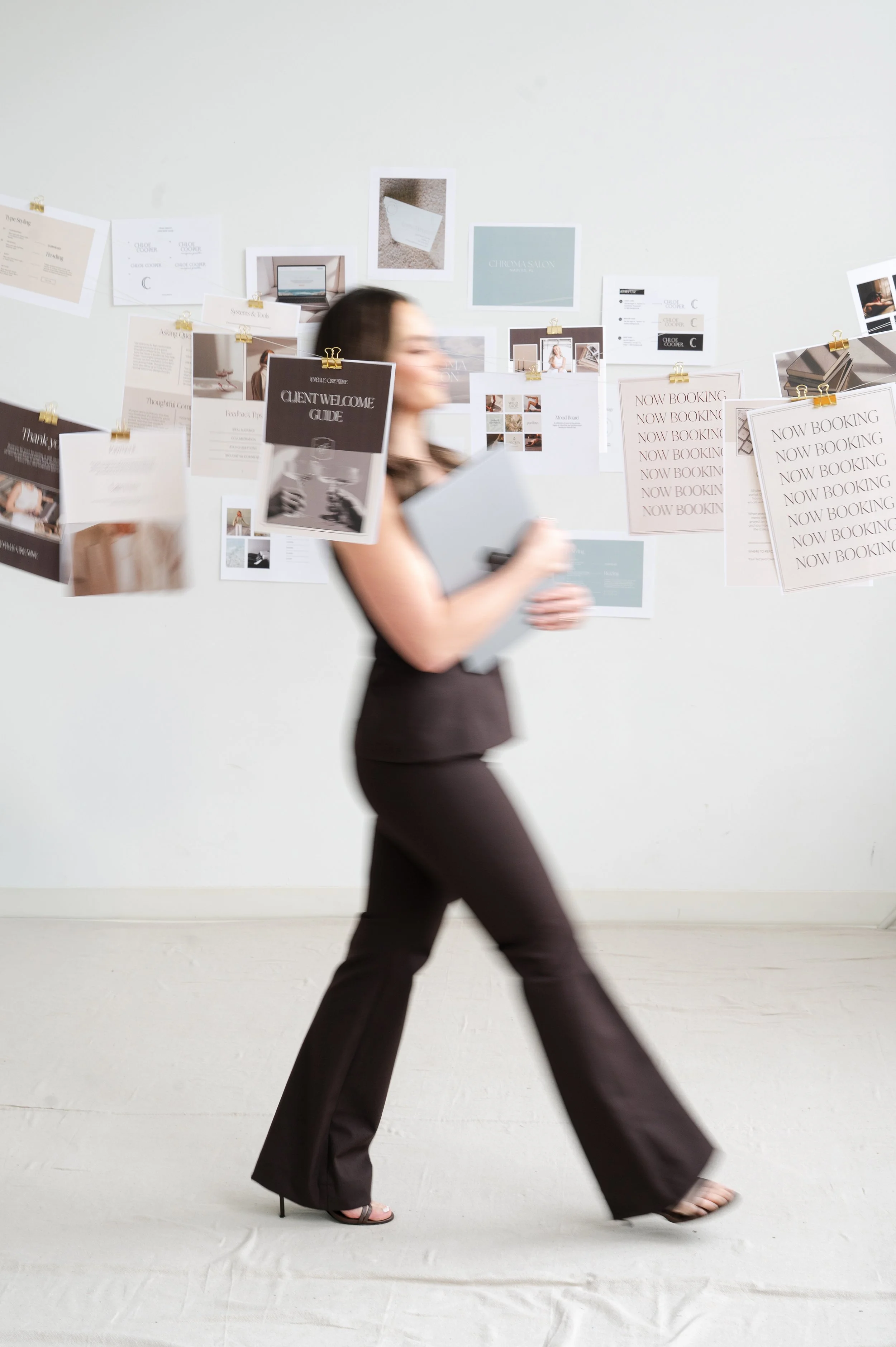 Abbey Delaney, owner of Evelle Creative, is wearing a brown outfit walking through photos of her brand and web design work hanging from fishing line.