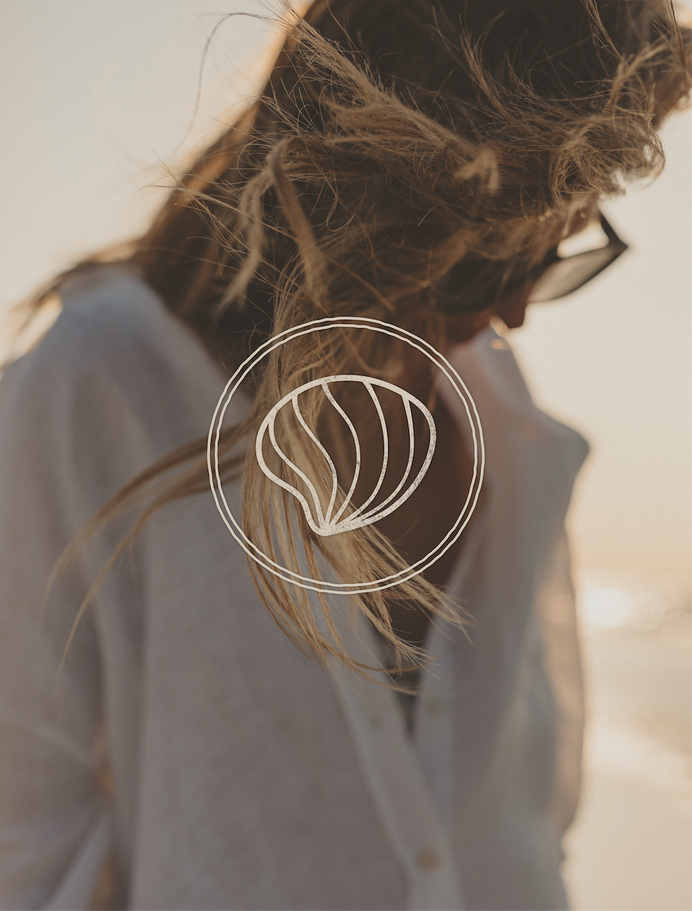 A woman with long blond hair and glasses looking down, outdoors during sunset.