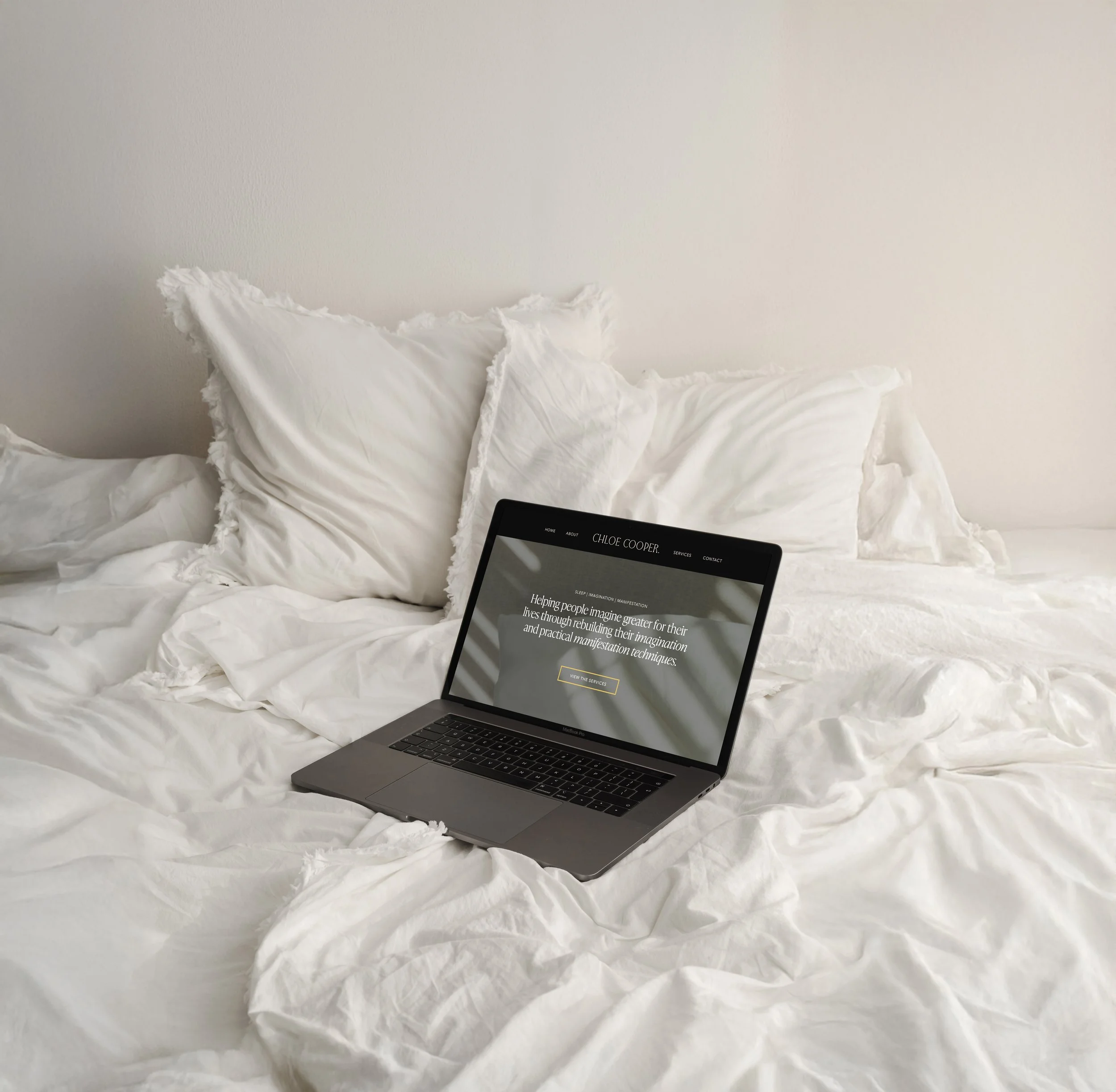Open laptop on a white bed with wrinkled sheets and pillows, displaying a website for Chloe Cooper that was designed by Evelle Creative.