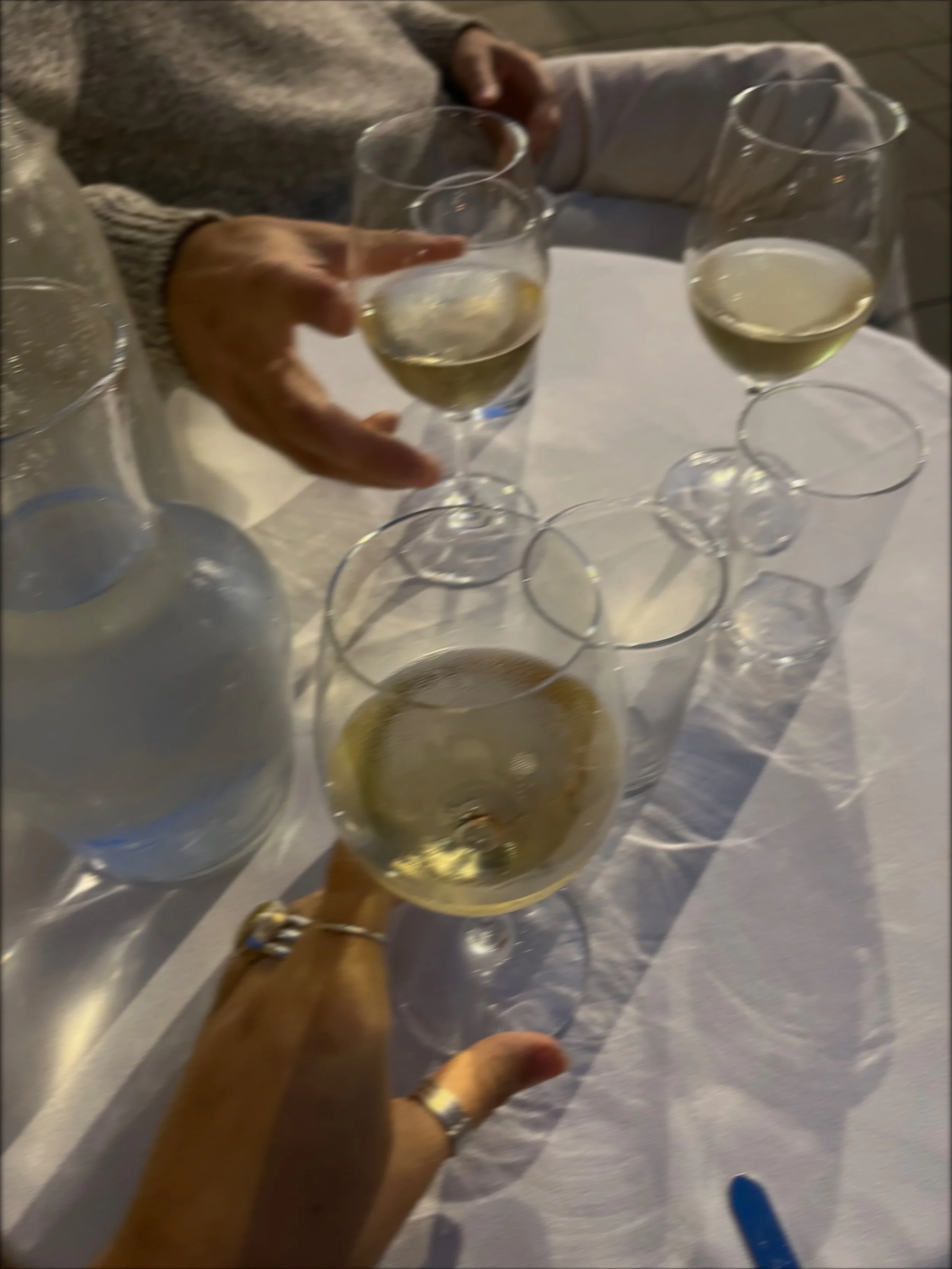 People clinking glasses of white wine at a dinner table with a white tablecloth.