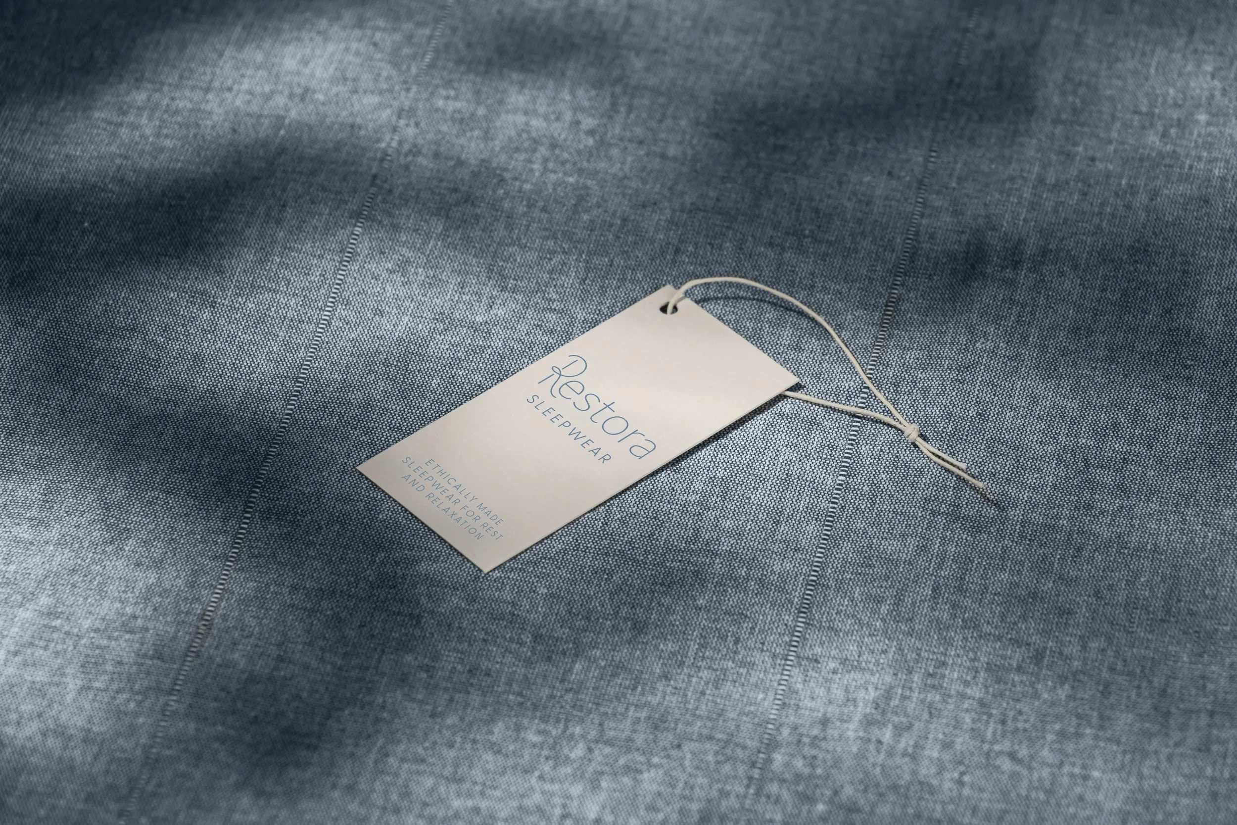 A clothing tag attached to a piece of sleepwear fabric. The tag reads 'Restora Sleepwear' and mentions it is ethically made for restful sleep and relaxation.