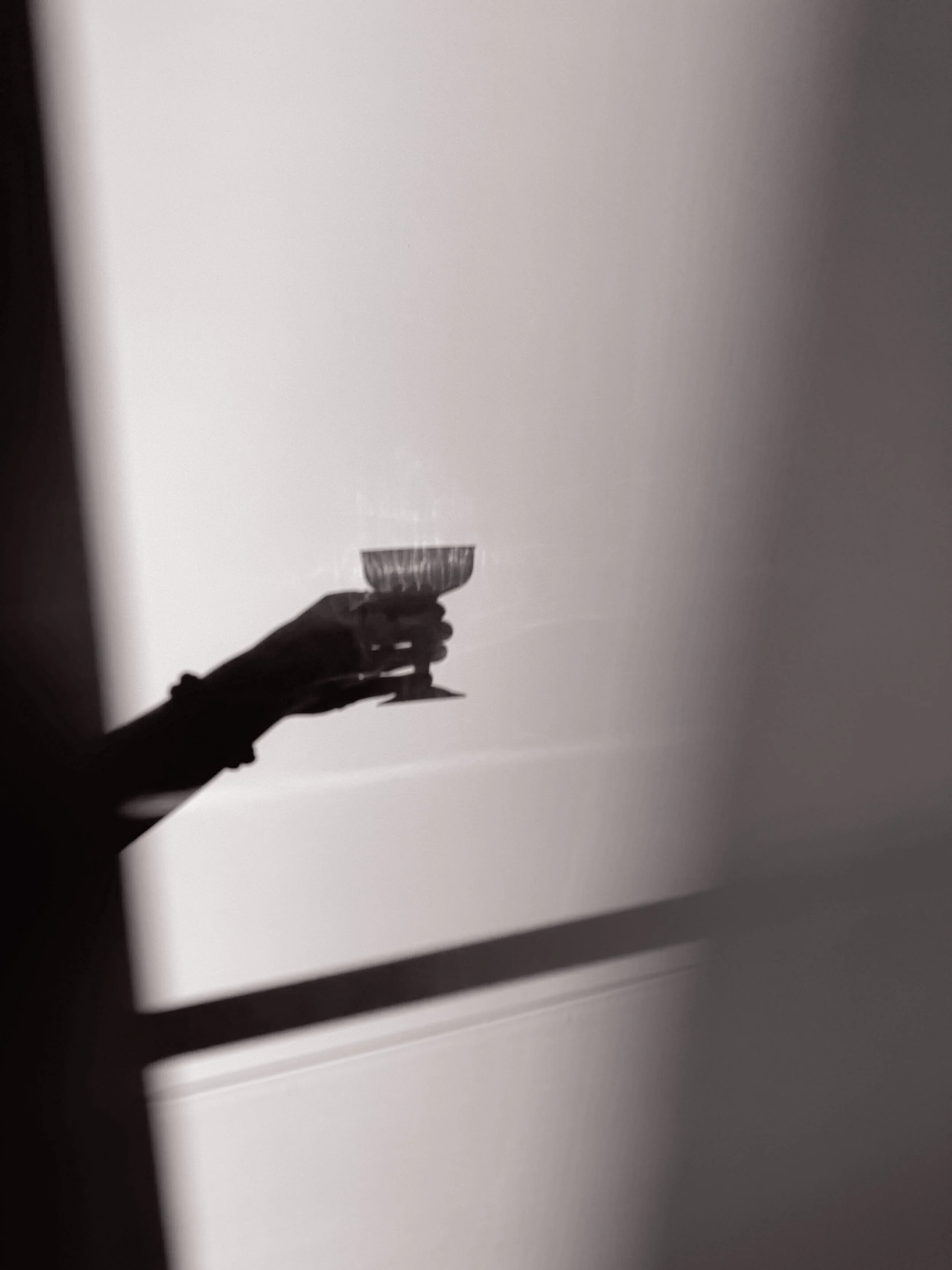 Shadow of a person's hand holding a glass of wine, reflected on a wall.