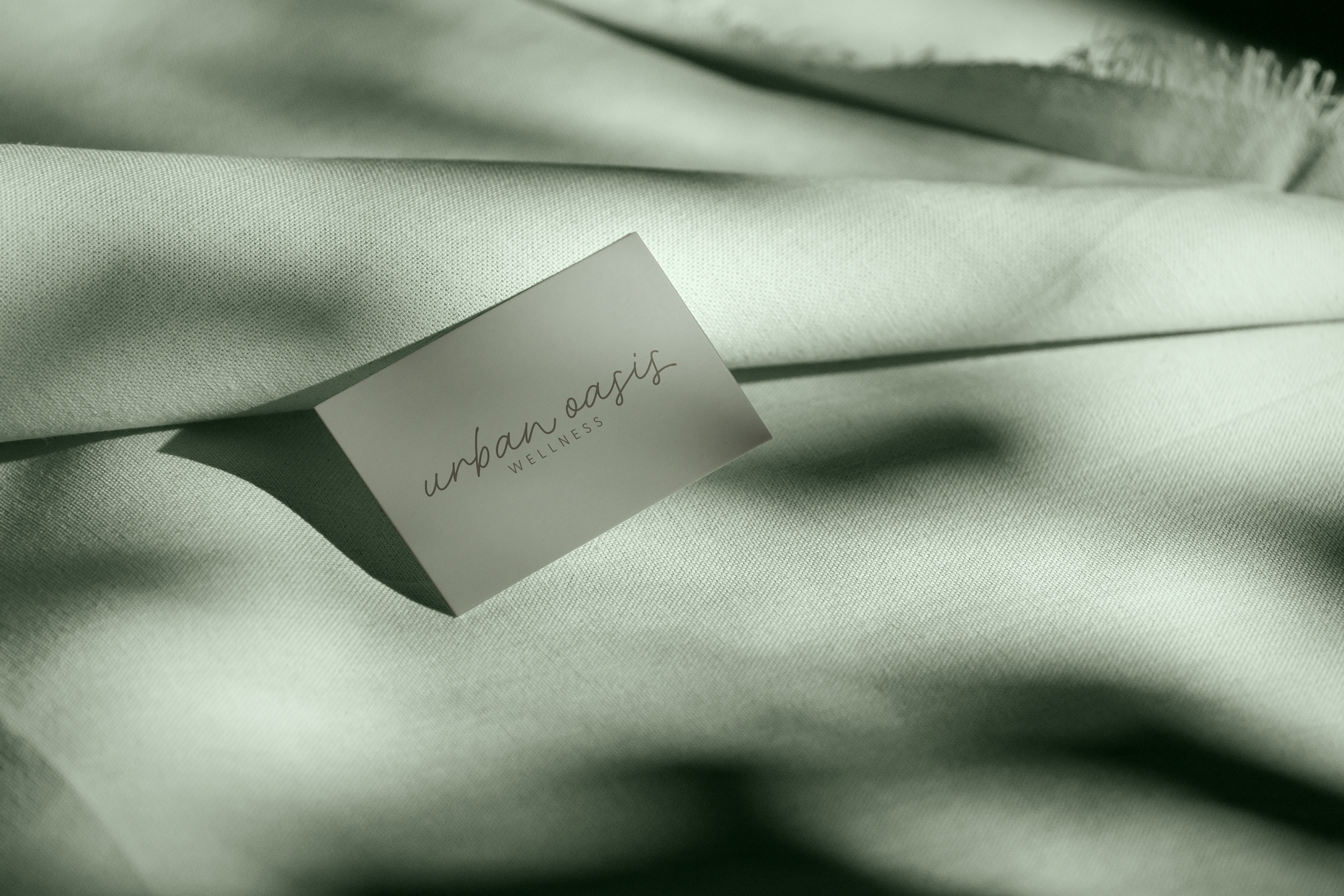 A white business card with the words 'urban oasis WELLNESS' lying on light green fabric.