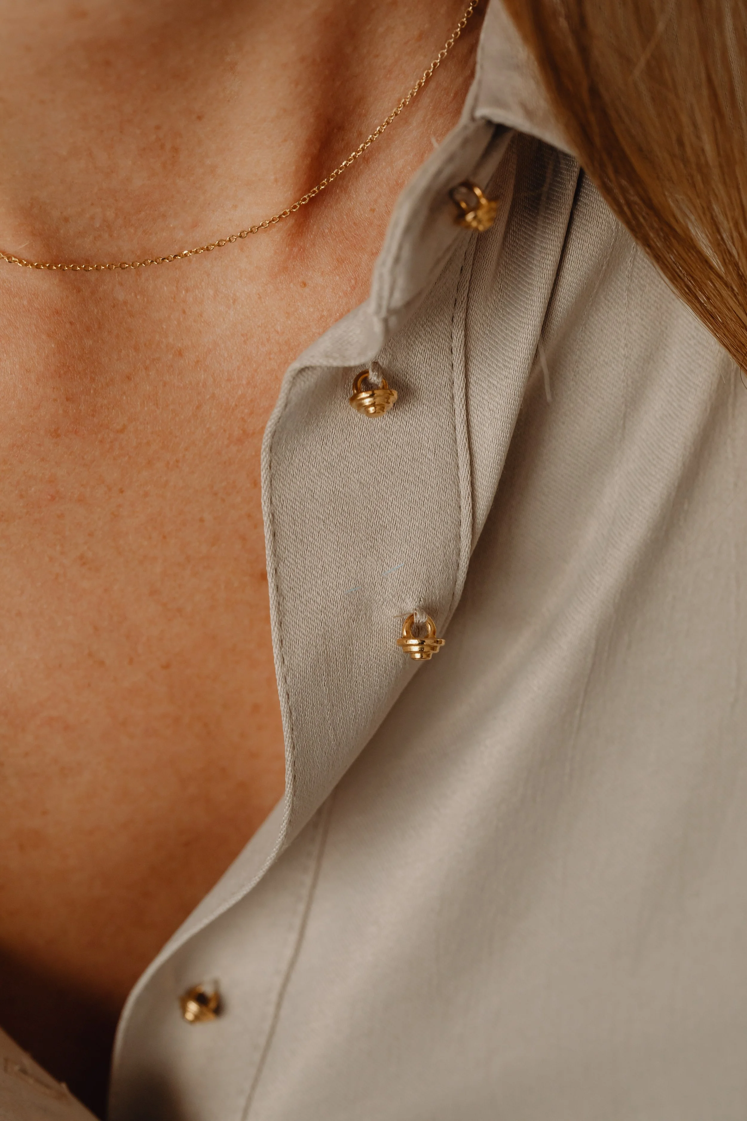 Close-up of a beige satin shirt with gold buttons and a gold chain necklace on a person's chest.