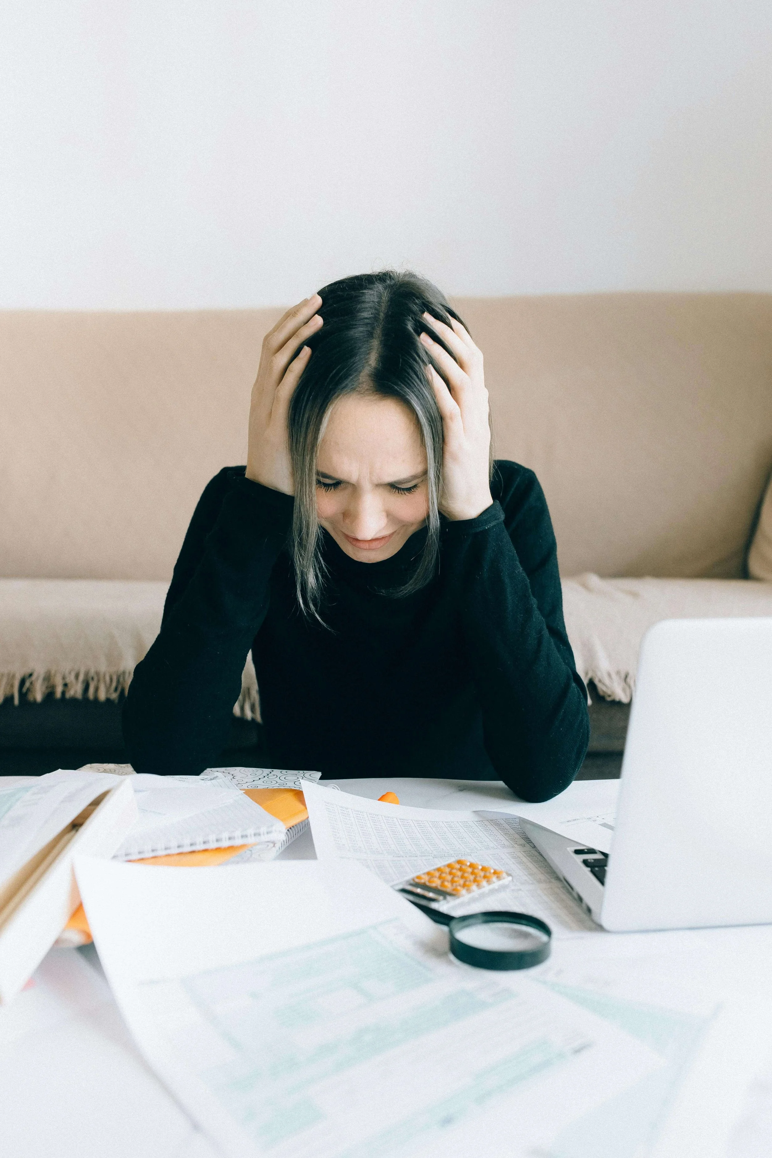 A professional woman holding her head in exhaustion by scattered papers. A burnout therapist in Bryant Park, NY can help you set work from home boundaries. Start your healing journey today.