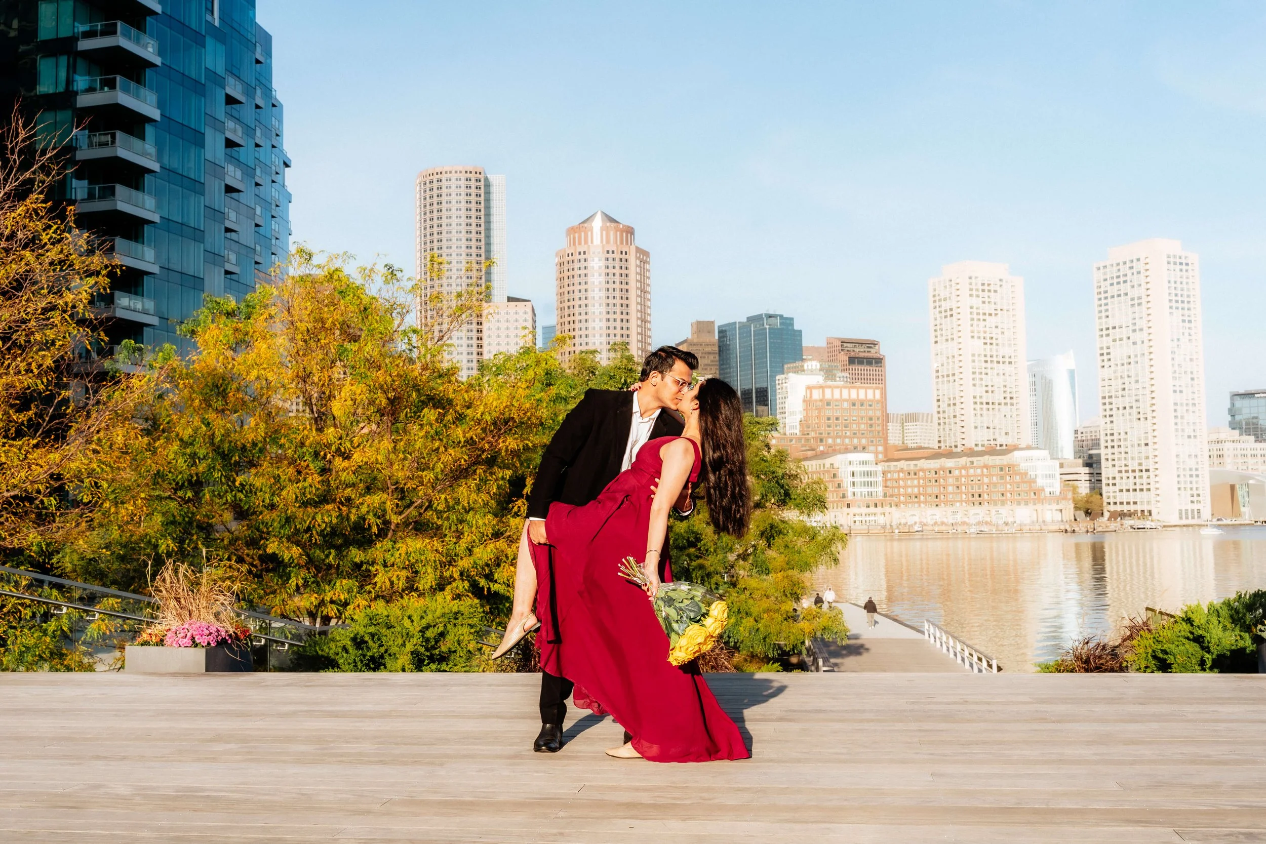 Couple embracing with Boston Seaport skyline during a summer morning couples photography session.