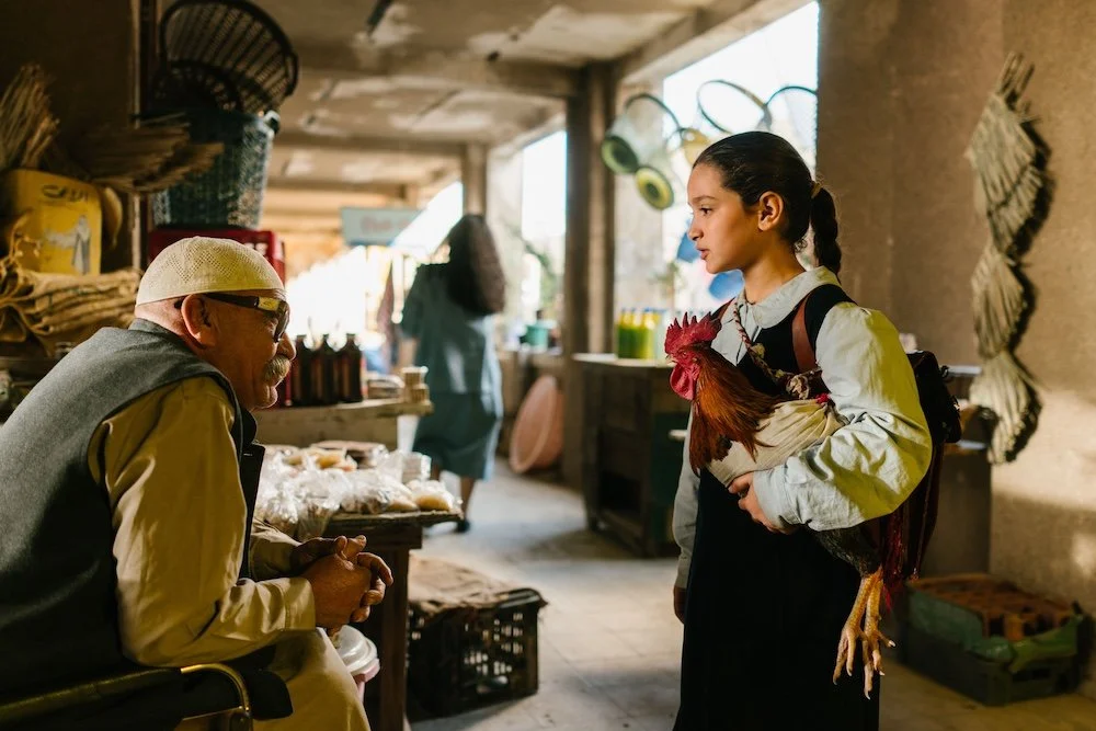 Film still of The President's Cake showing a young girl holding her pet cockerel and talking to a market seller