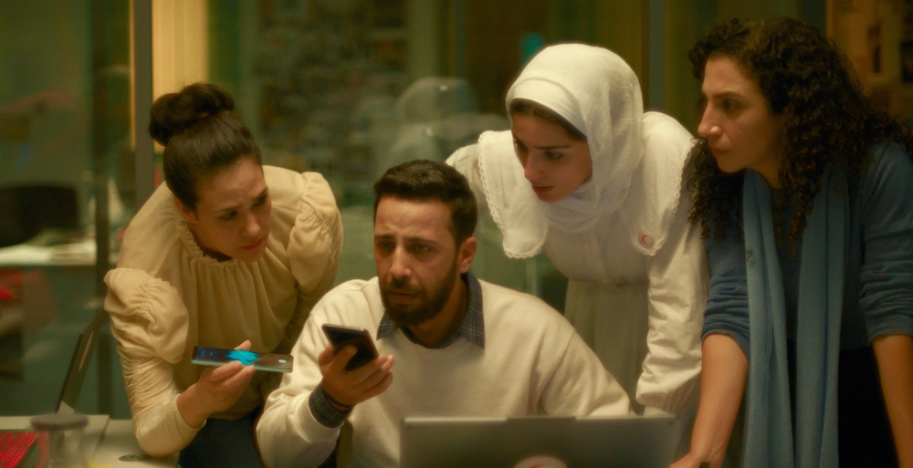 A film still from The Voice of Hind Rajab showing four people around a phone and desk, looking concerned