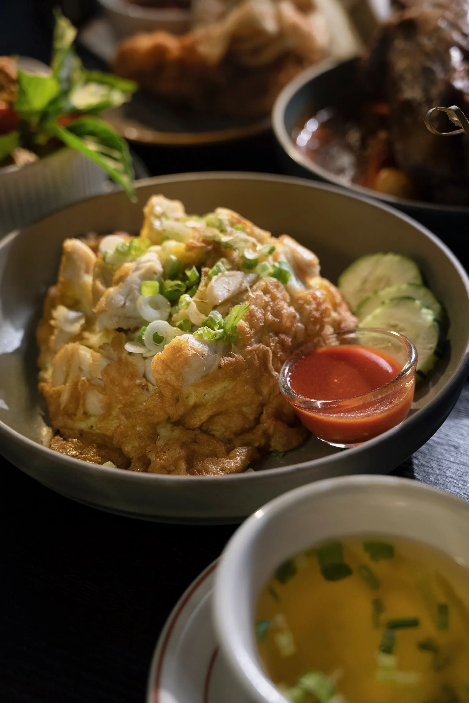 Egg omelet with jumbo lump crab meat and green onions, side of cucumbers and Thai sriracha sauce, partial view of vegetable broth on the side