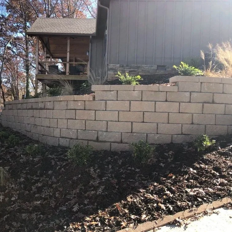 A tiered stone retaining wall on a grassy slope featuring integrated drainage pipes to prevent soil erosion and water runoff.