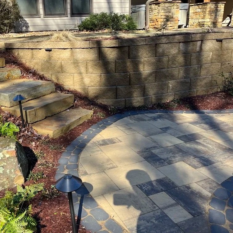 Illustration of a stepped stone retaining wall on a graded slope with a gravel drainage base and professional landscaping tools.