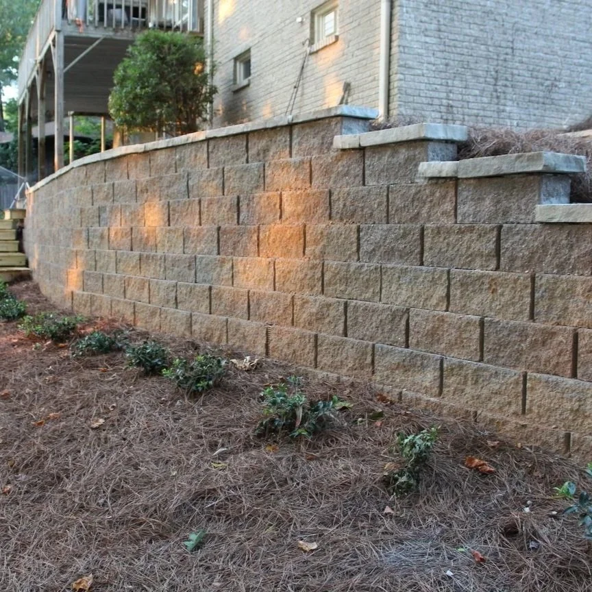 A multi-level segmental retaining wall built with textured grey stone blocks, stabilizing a sloped residential yard with integrated landscape planting.