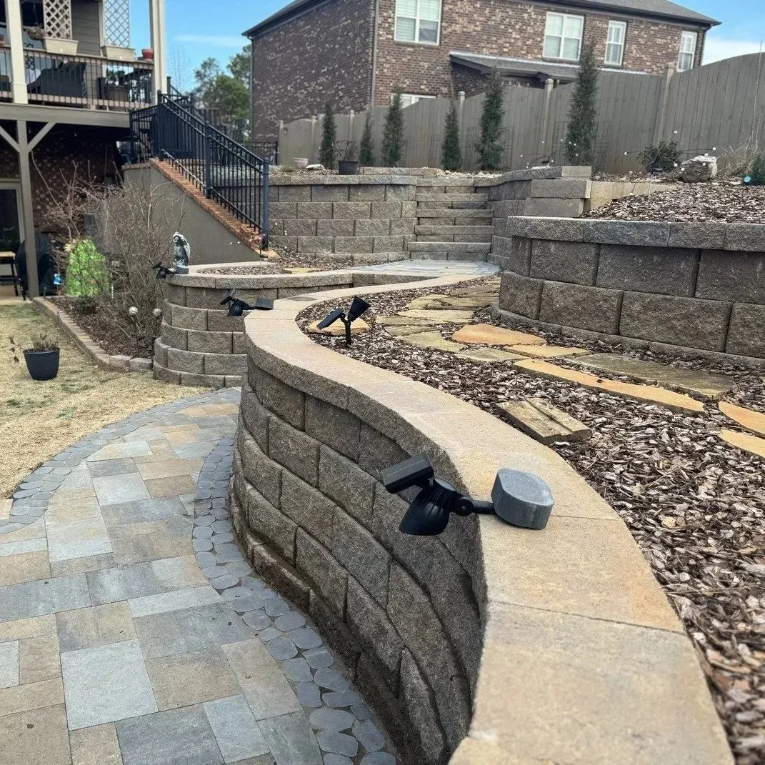 A sturdy stone retaining wall stabilizing a sloped residential yard, preventing soil erosion and creating a flat, functional landscape.