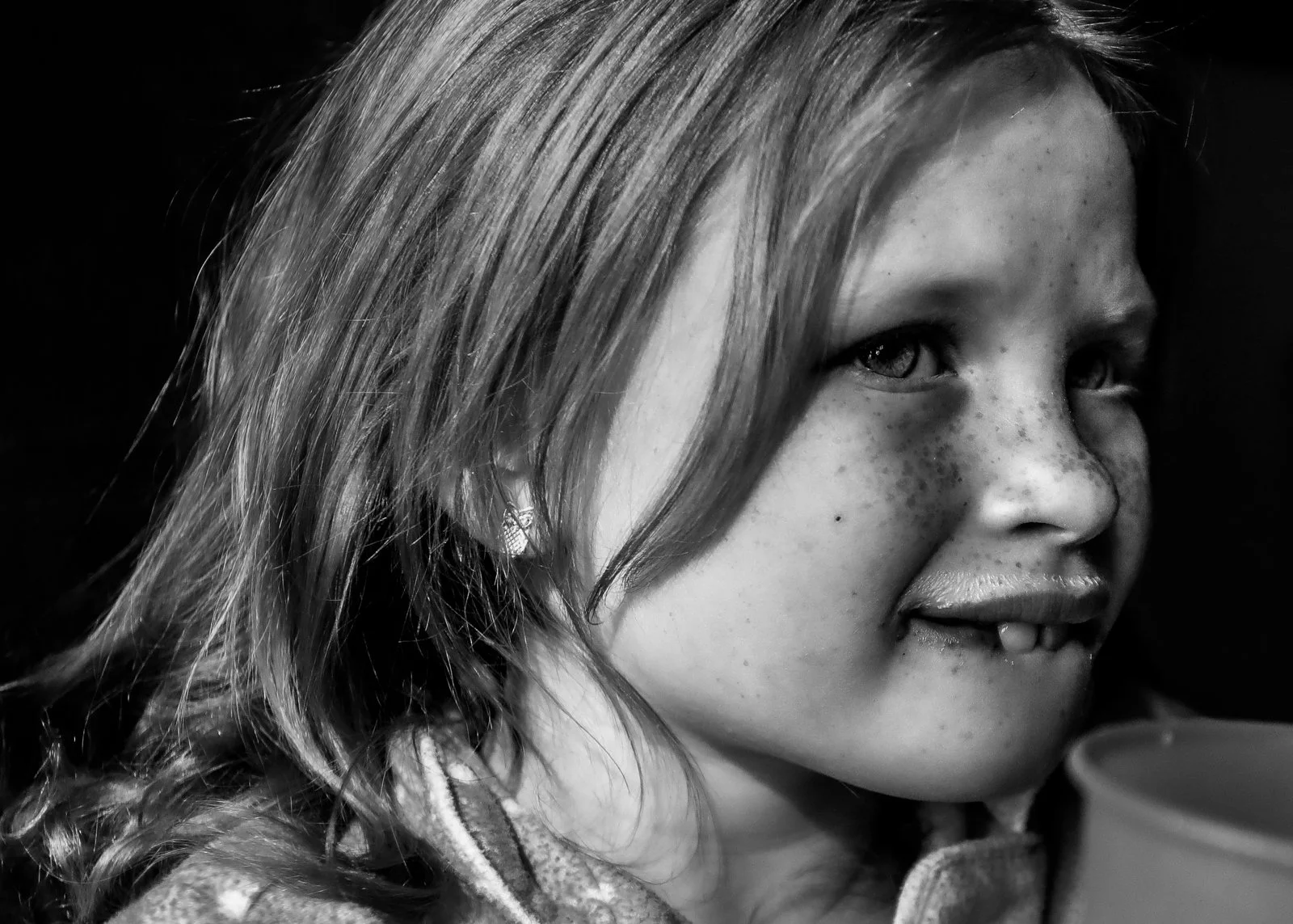 A young girl with light-colored hair and freckles, looking to her right, holding a cup with a lid.