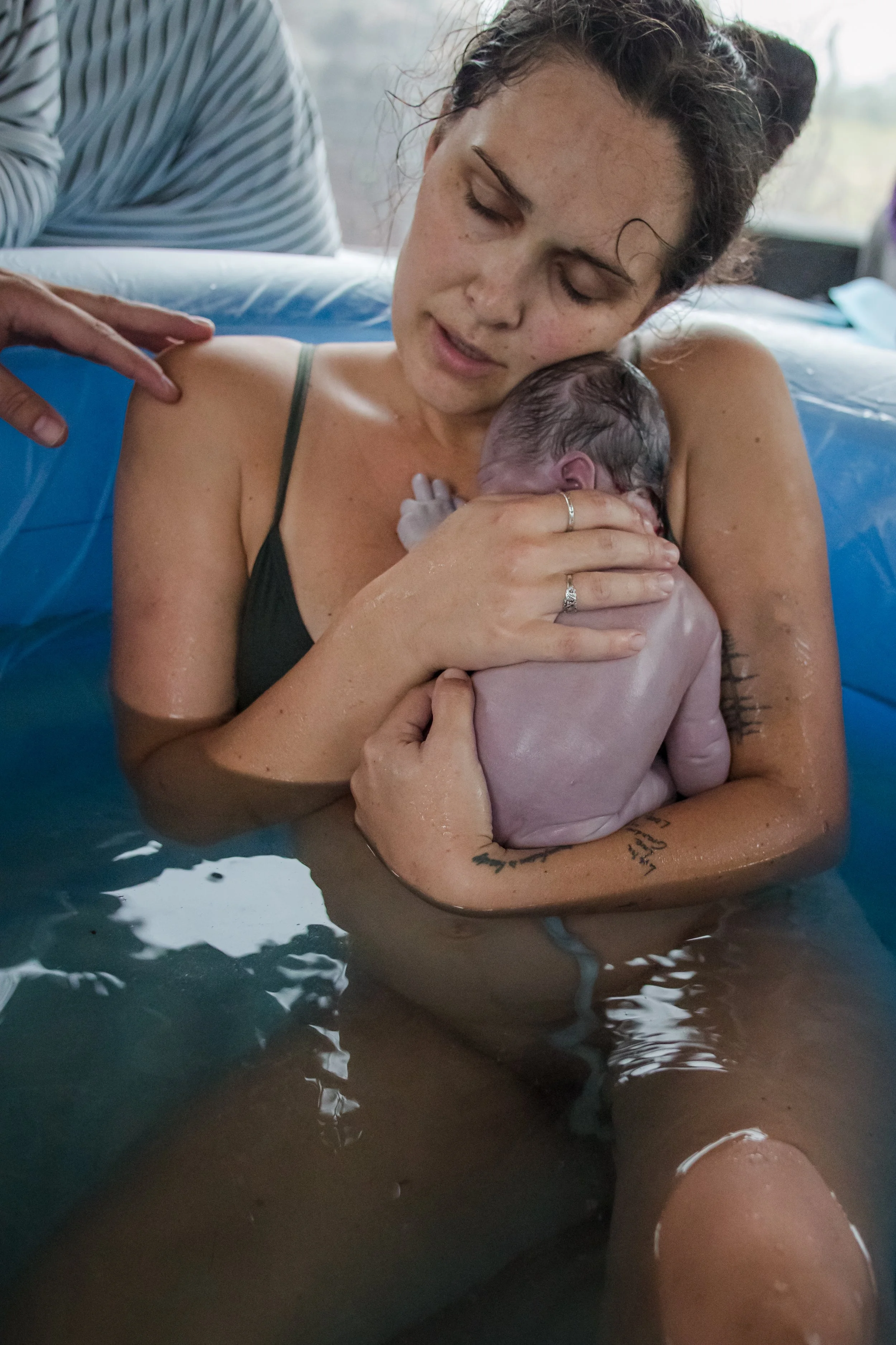 A woman is holding a newborn baby in a water birth, with gentle expressions; she is in a birthing pool surrounded by medical staff.