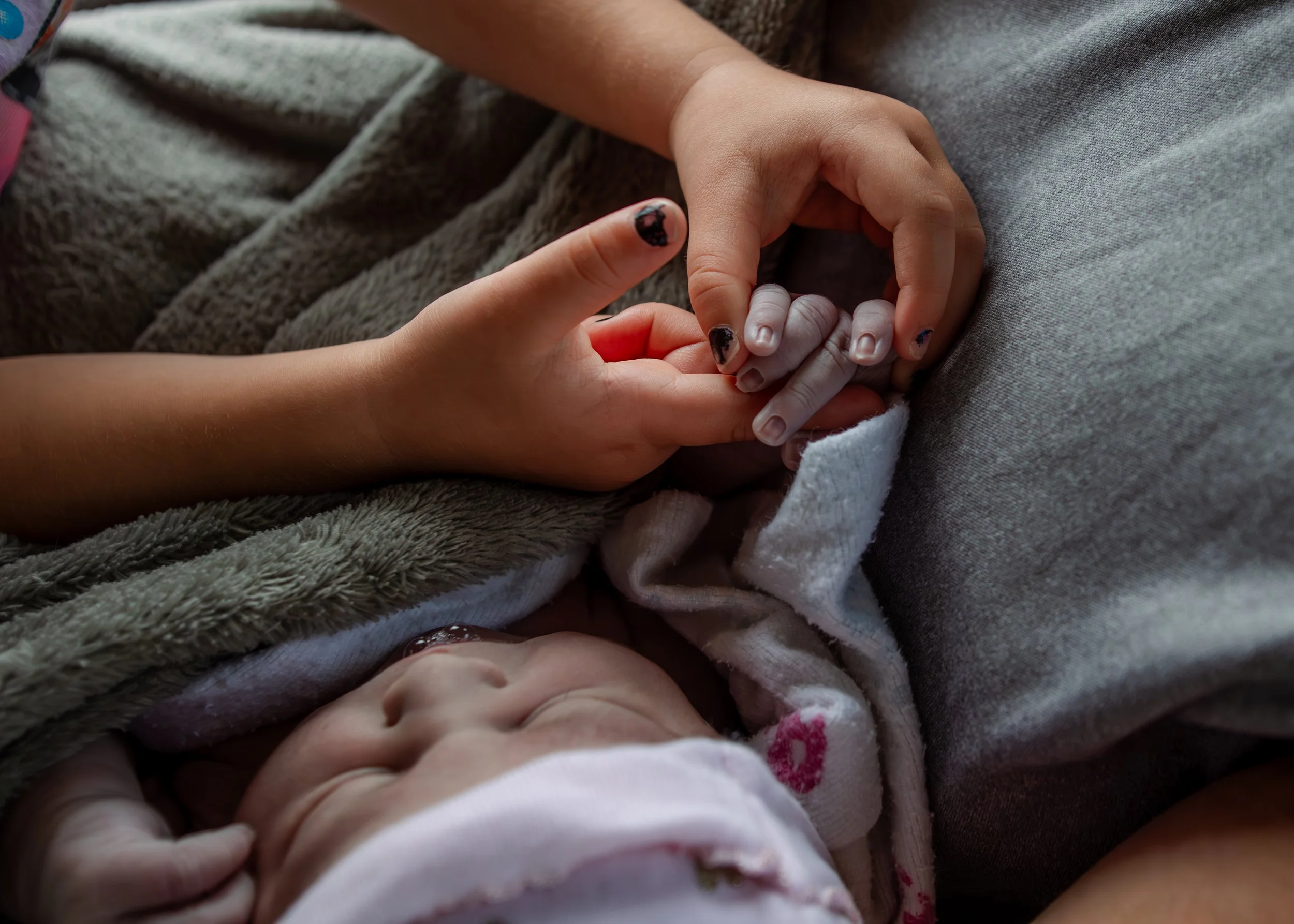 A newborn baby sleeping with a mother holding baby's hand gently.
