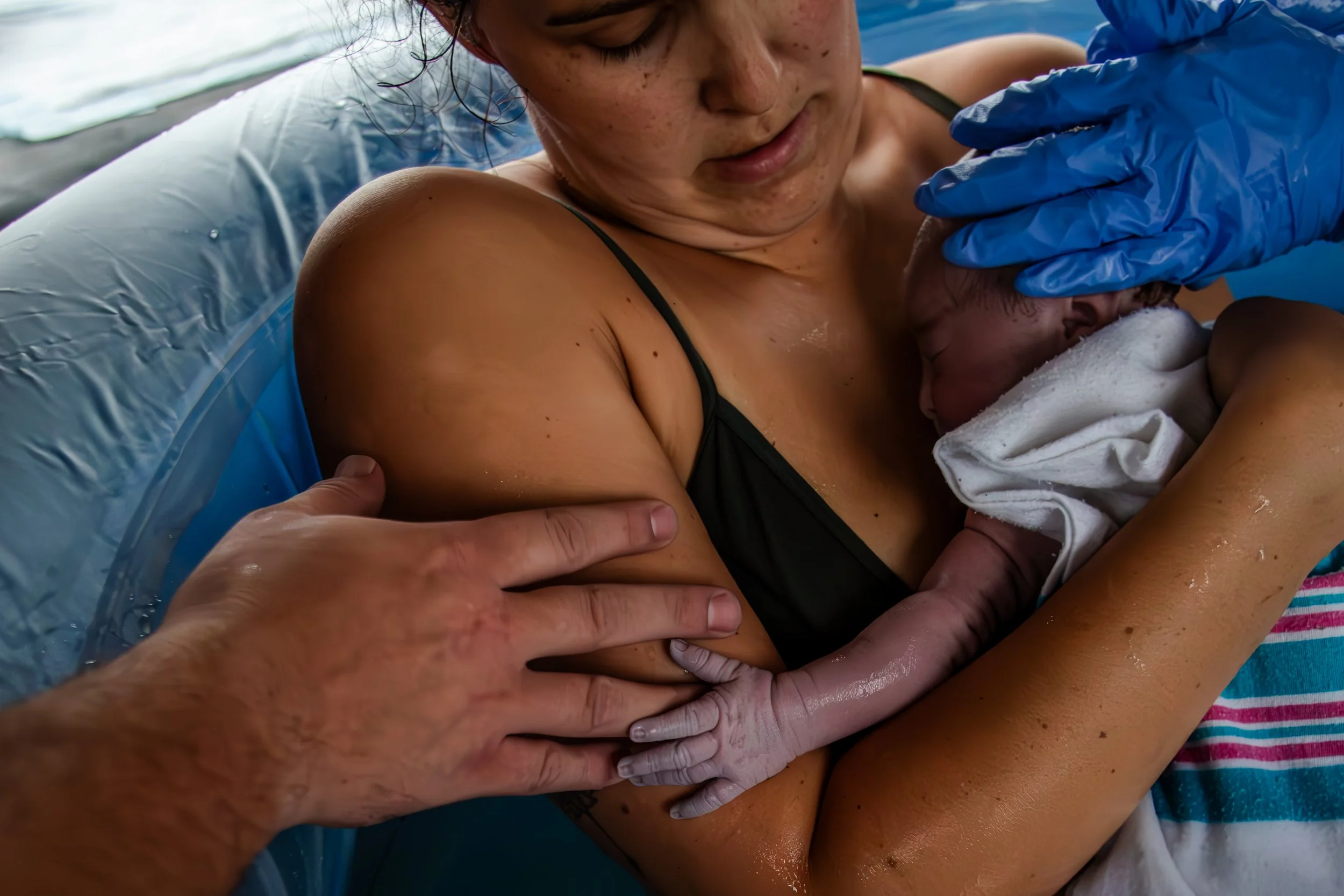 A woman holding a newborn baby after childbirth, with medical personnel assisting, in a hospital delivery room.