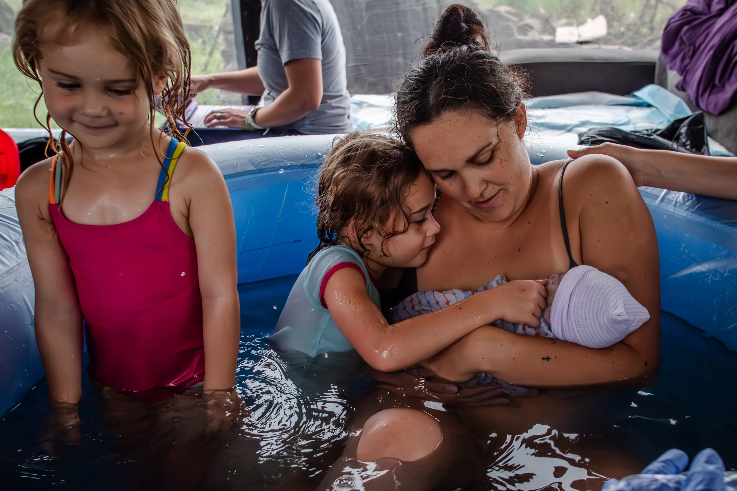 A woman, two young girls, and a baby in a makeshift baptismal pool inside a vehicle, likely during a baptism ceremony.
