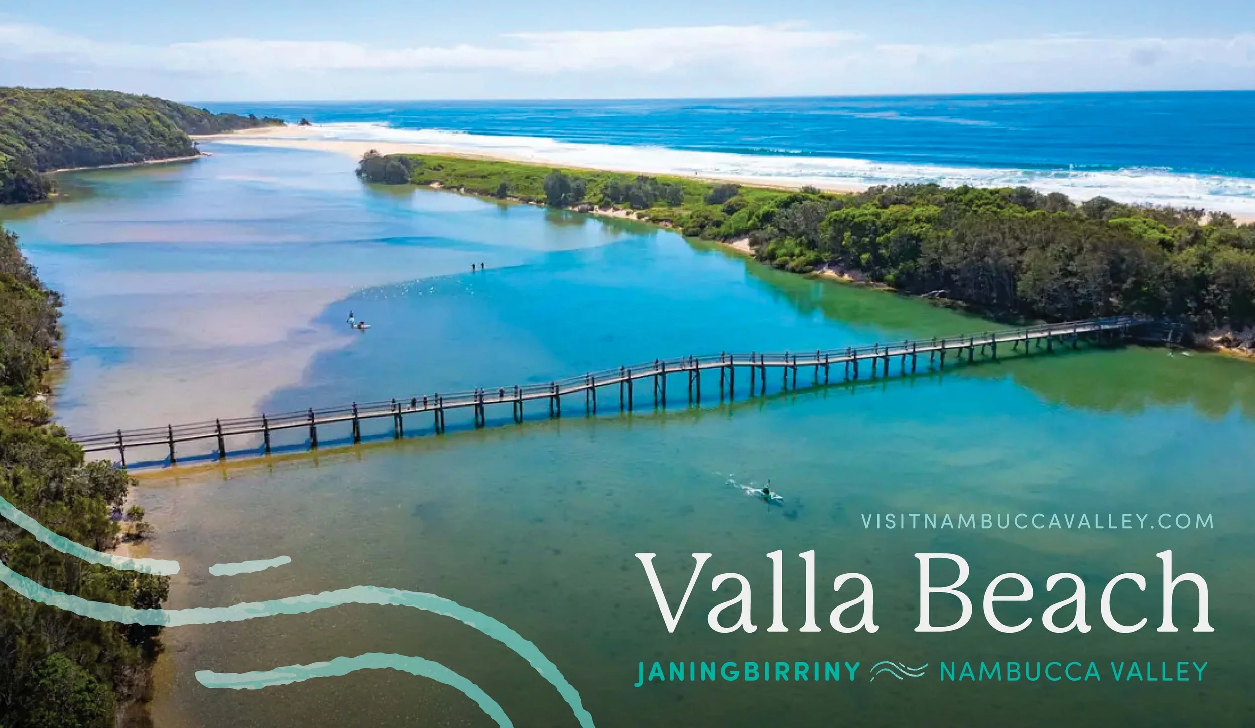 A scenic view of Valla Beach showing a river meeting the ocean, with a wooden bridge crossing the river, surrounded by lush green trees, with people paddleboarding and kayaking, under a partly cloudy sky.