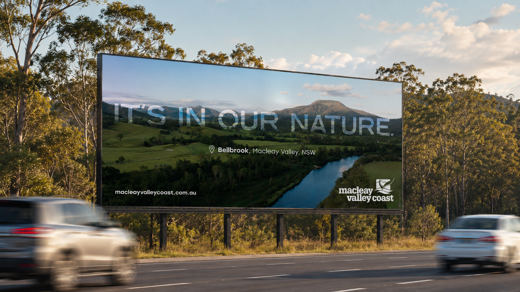 Billboard advertising Bellbrook in Macleay Valley, NSW, featuring a scenic landscape with a river, green hills, and mountains under a partly cloudy sky.