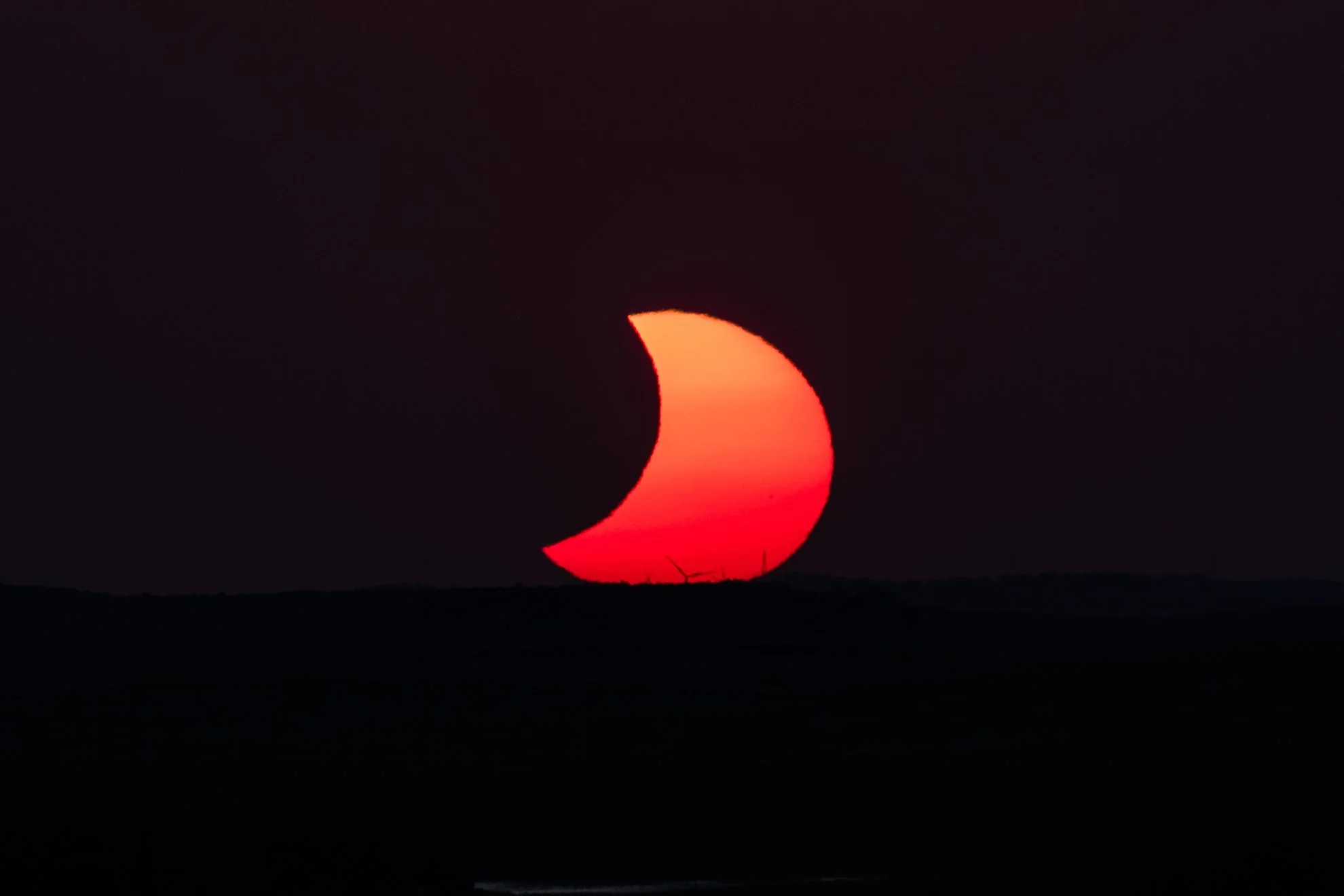 Partially eclipsed sun setting over some windmills.