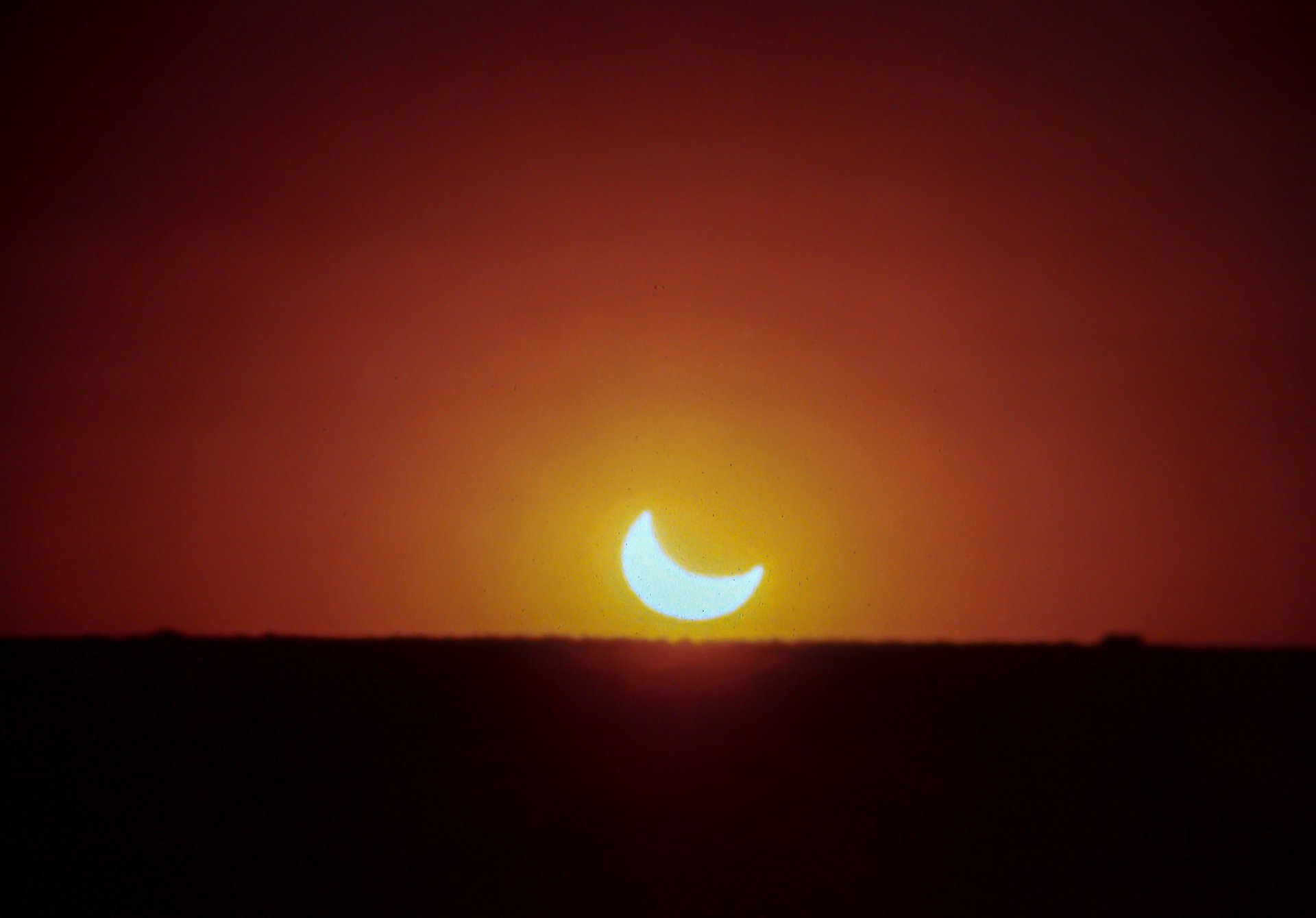 The partially eclipse sun slips over the horizon.