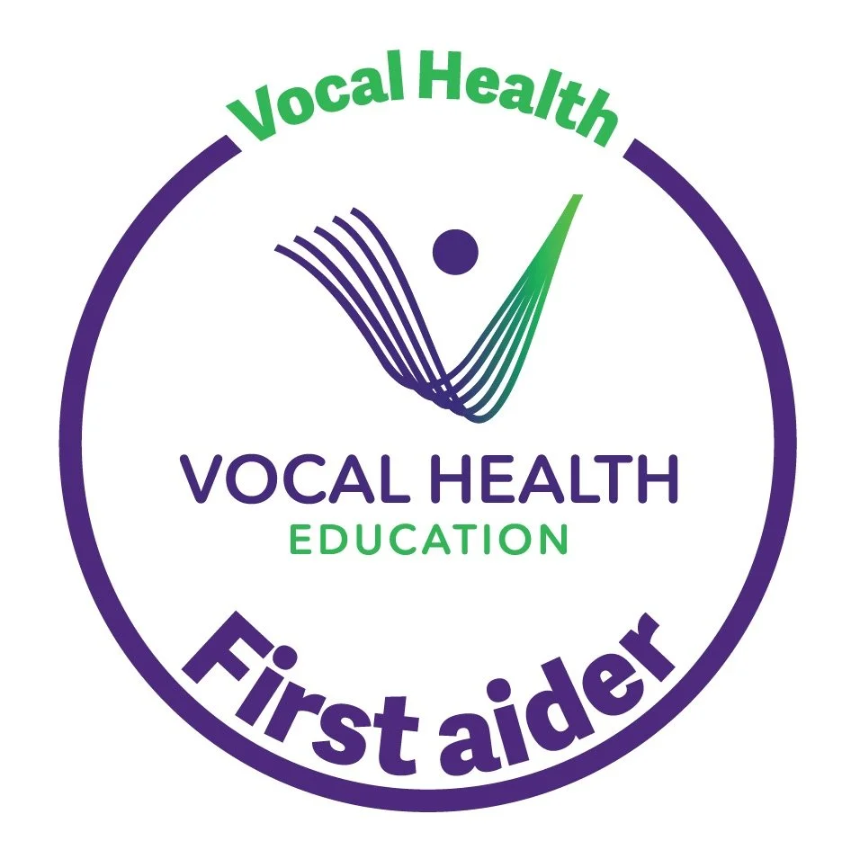 A circular logo with a purple border and text. Green text reads 'Vocal Health' at the top and 'First aider' at the bottom. Inside, purple text says 'Vocal Health' and green text says 'Education'. There is a stylized graphic of vocal cords and a dot r