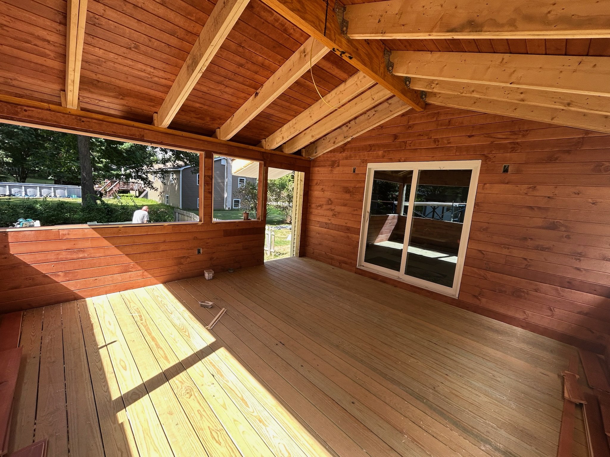 Interior of a house under construction with wood framed ceiling, wooden walls, and a sliding glass door leading outside.
